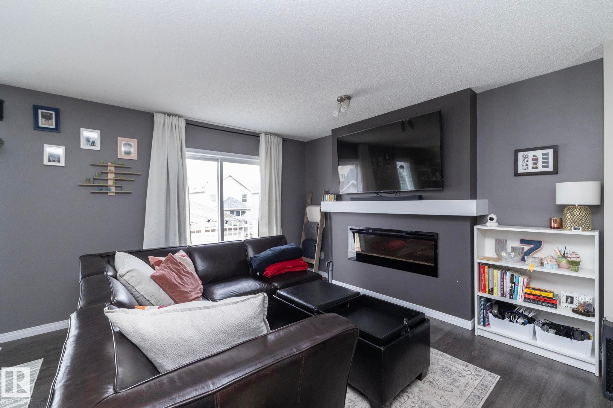 Living area featuring a modern linear electric fireplace with a white mantel, dark wood-finish flooring, and a large sliding glass door - 46 4050 Savaryn Drive, Edmonton, AB