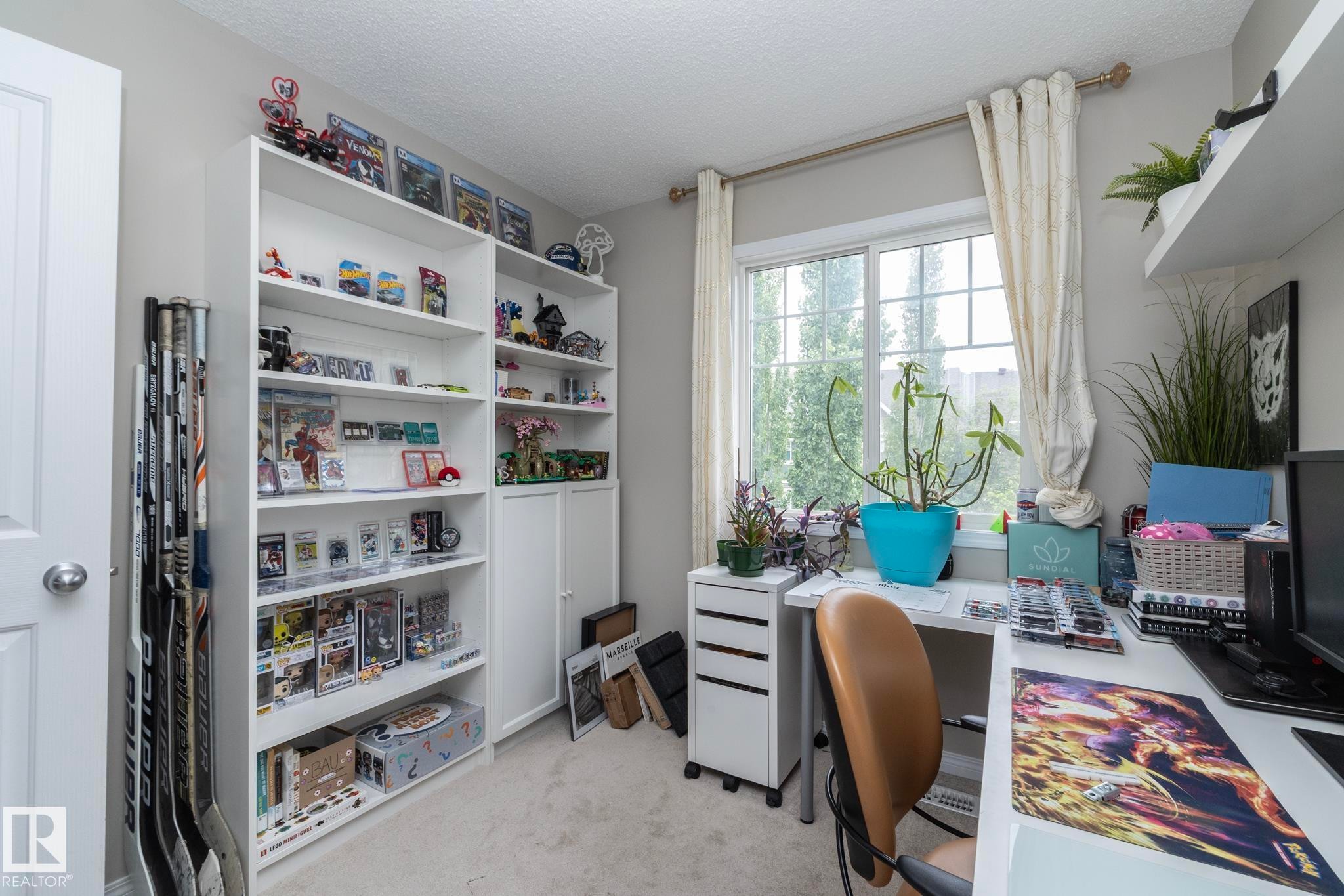 Room featuring neutral wall paint, carpet flooring, a large window with vertical muntins, and built-in white shelving units - 46 4050 Savaryn Drive, Edmonton, AB