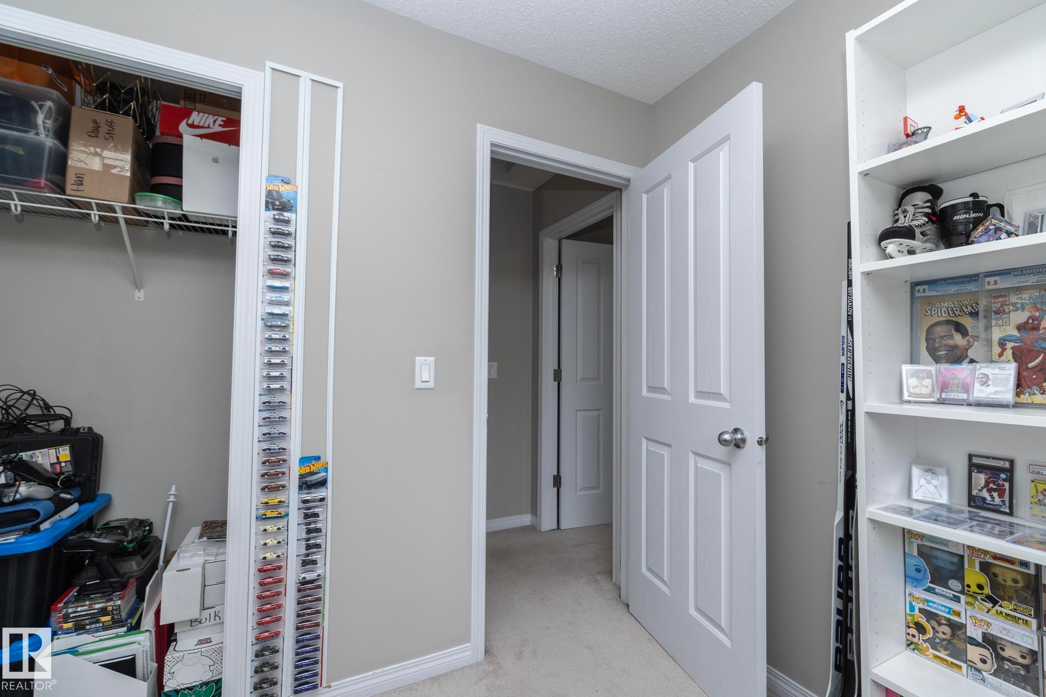 Interior hallway featuring a closet with wire shelving, carpet flooring, a built-in white bookshelf, and an interior door with a silver-tone knob - 46 4050 Savaryn Drive, Edmonton, AB