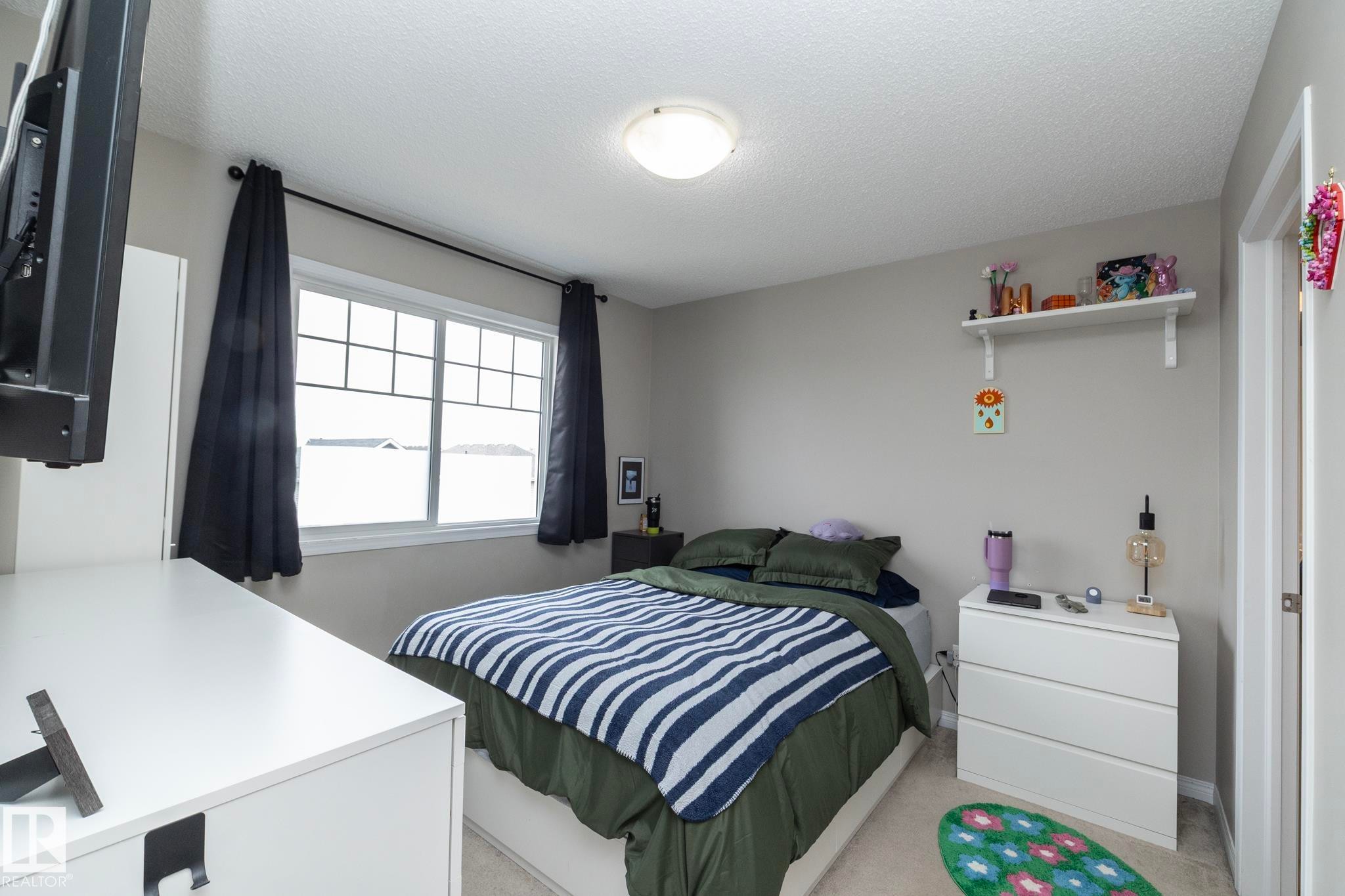 Windowed bedroom featuring neutral wall paint, carpet flooring, a ceiling-mounted light fixture, and a built-in wall shelf - 46 4050 Savaryn Drive, Edmonton, AB