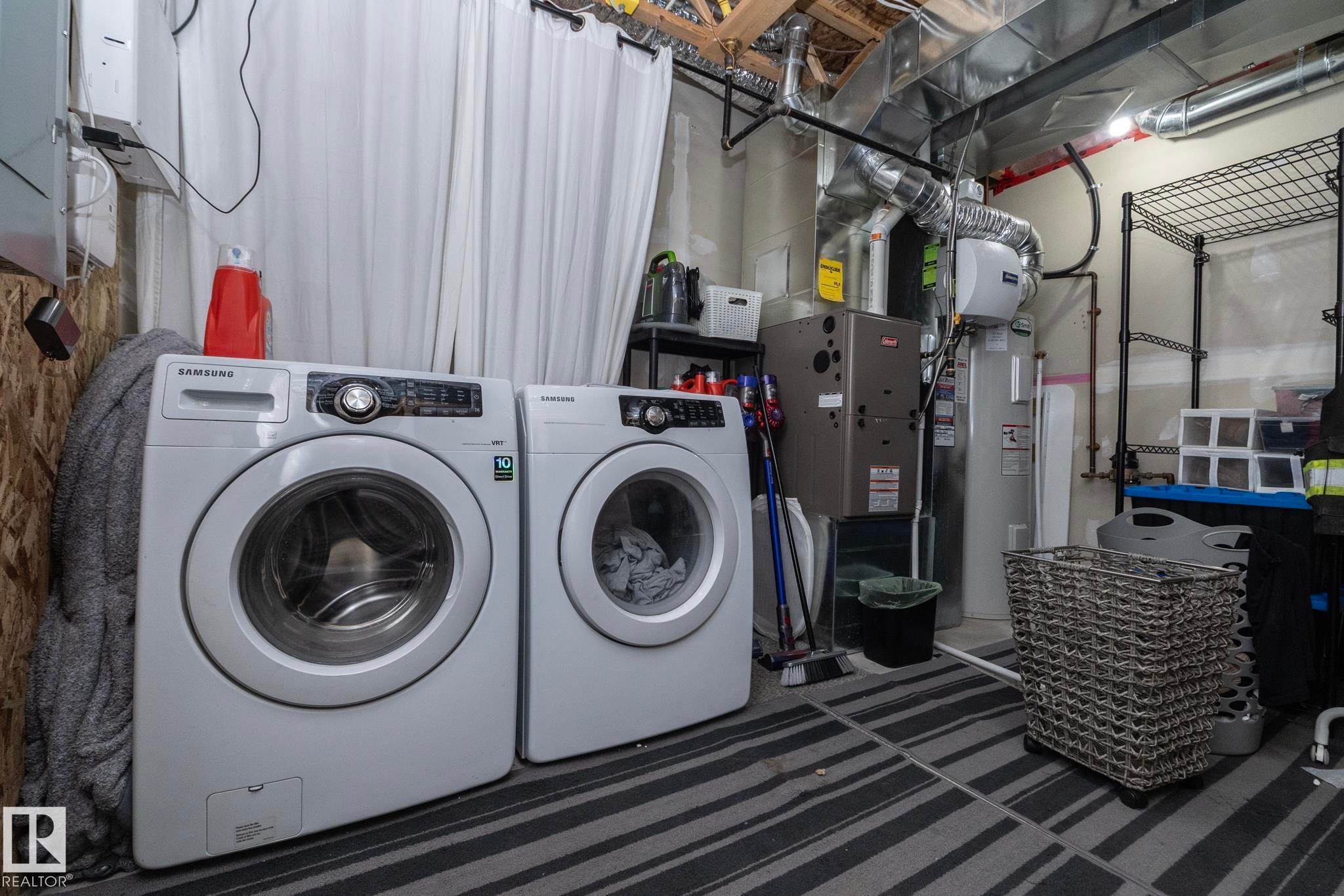 Dedicated laundry area featuring a front-loading washer and dryer, exposed ceiling joists, utility shelving, and a water heater - 46 4050 Savaryn Drive, Edmonton, AB