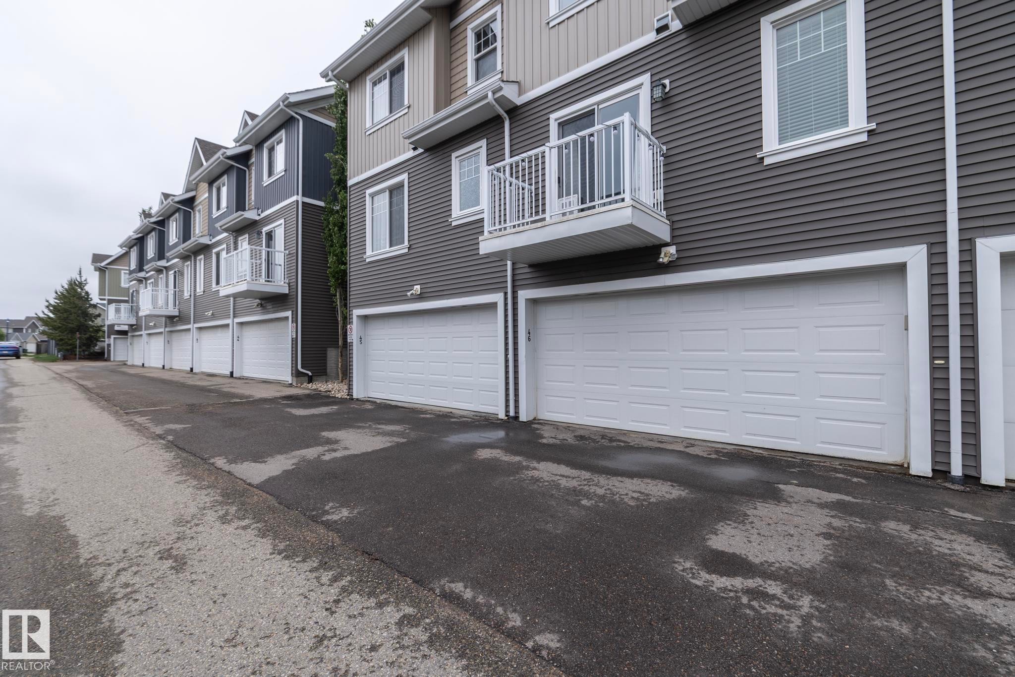 Modern townhome exterior featuring multi-toned siding, a panel garage door, a white-railed balcony, and white-framed windows - 46 4050 Savaryn Drive, Edmonton, AB
