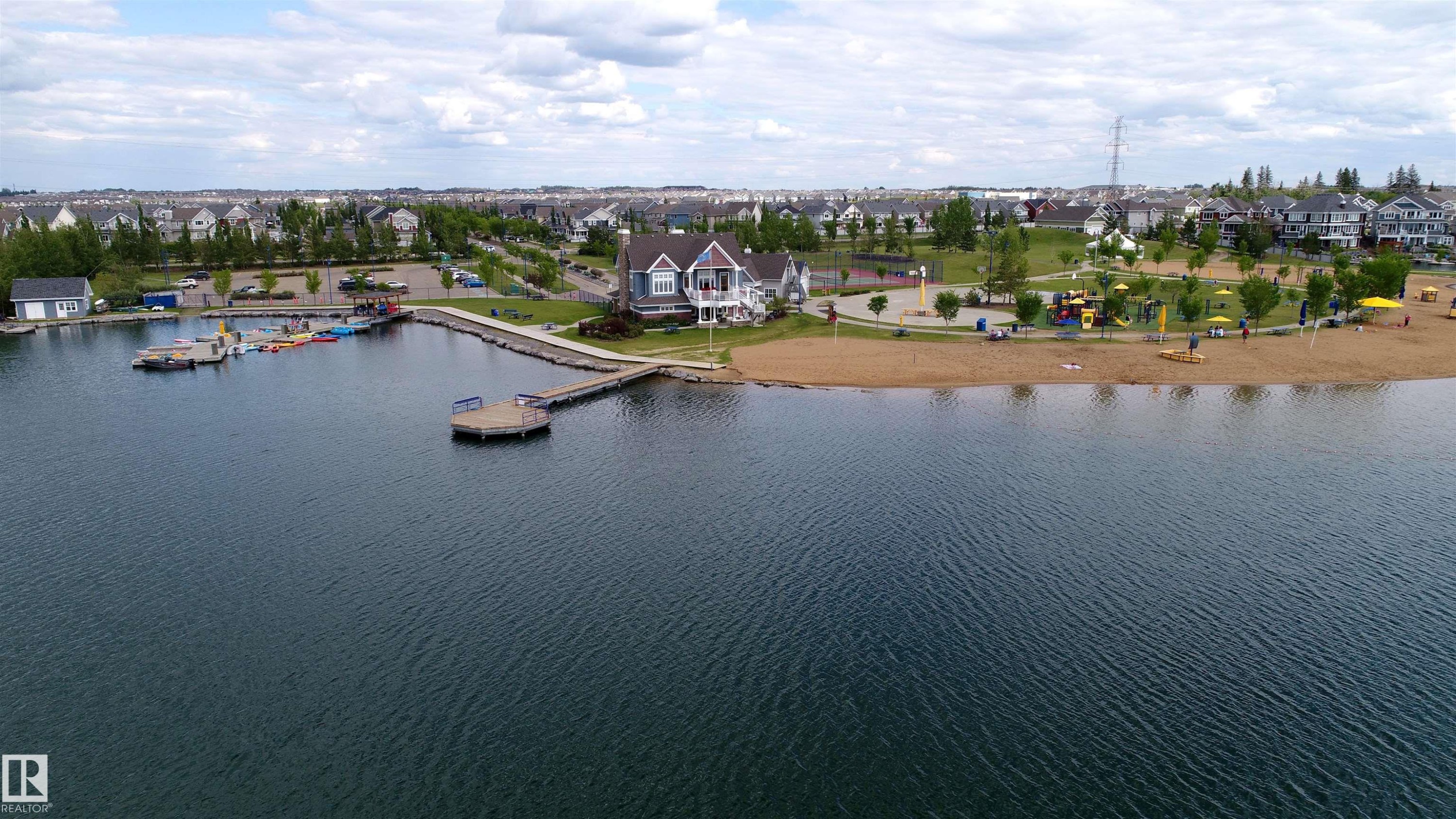 Lakefront property featuring a private dock, sandy beach, waterside building, and playground amenities - 46 4050 Savaryn Drive, Edmonton, AB