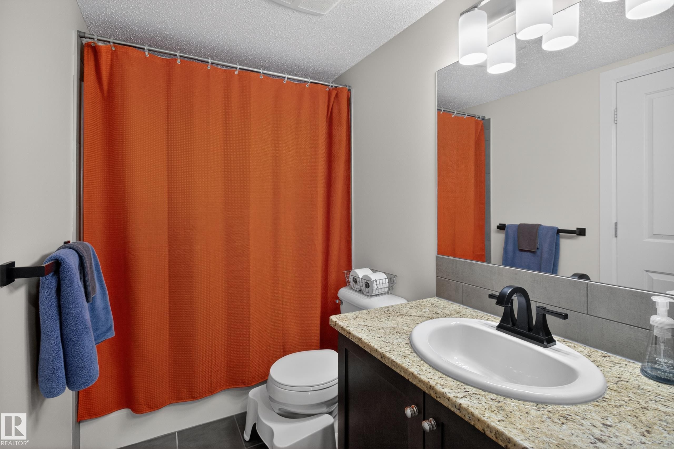Full bathroom featuring a dark wood-finish vanity with a granite-look countertop and an integrated white oval sink - 211 3719 Whitelaw Lane, Edmonton, AB