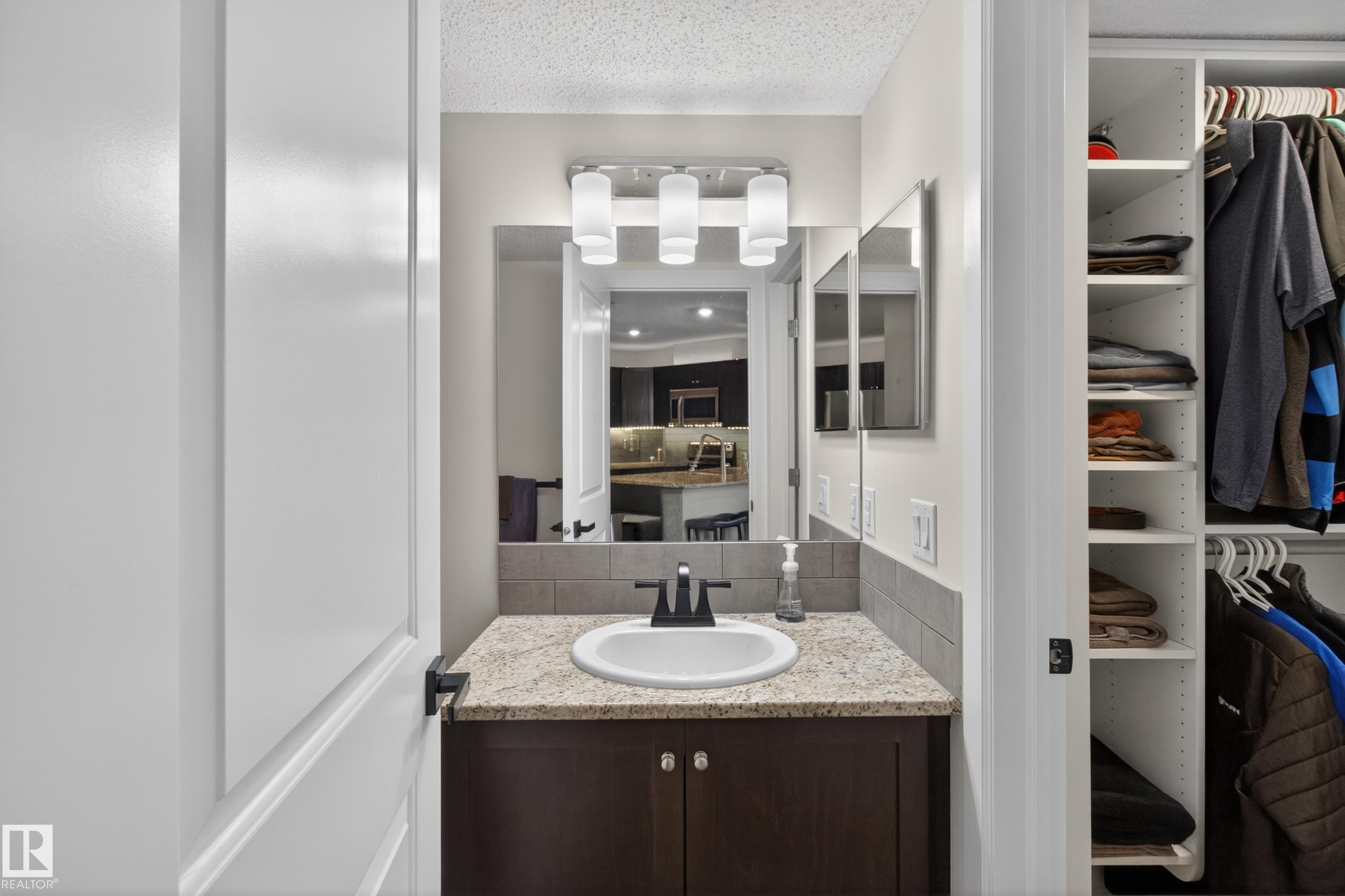 Bathroom vanity featuring a granite-style countertop, undermount sink, dark wood-finish cabinetry, and a tile backsplash - 211 3719 Whitelaw Lane, Edmonton, AB
