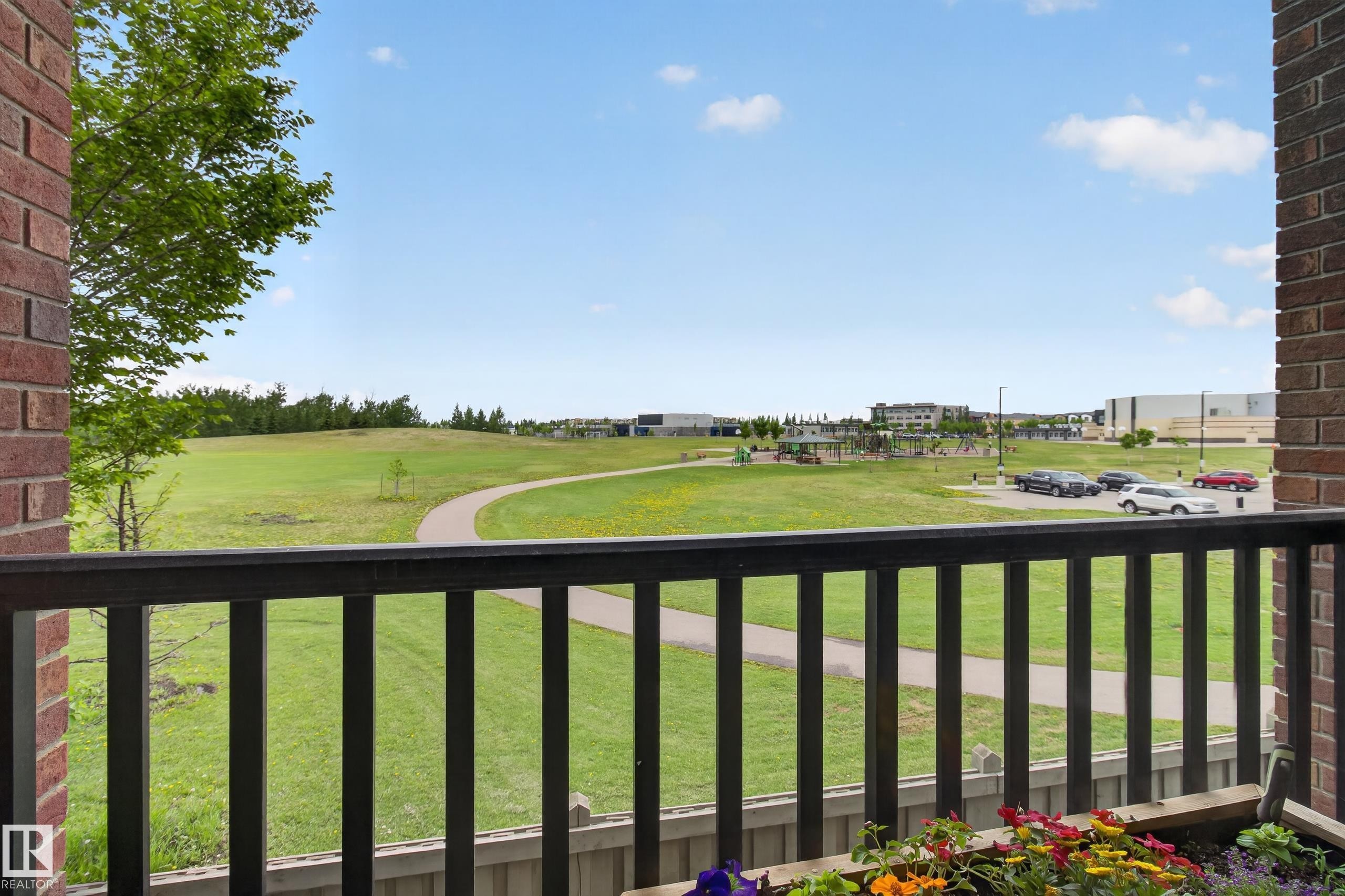 Expansive green space featuring a paved walking path and a distant playground - 211 3719 Whitelaw Lane, Edmonton, AB