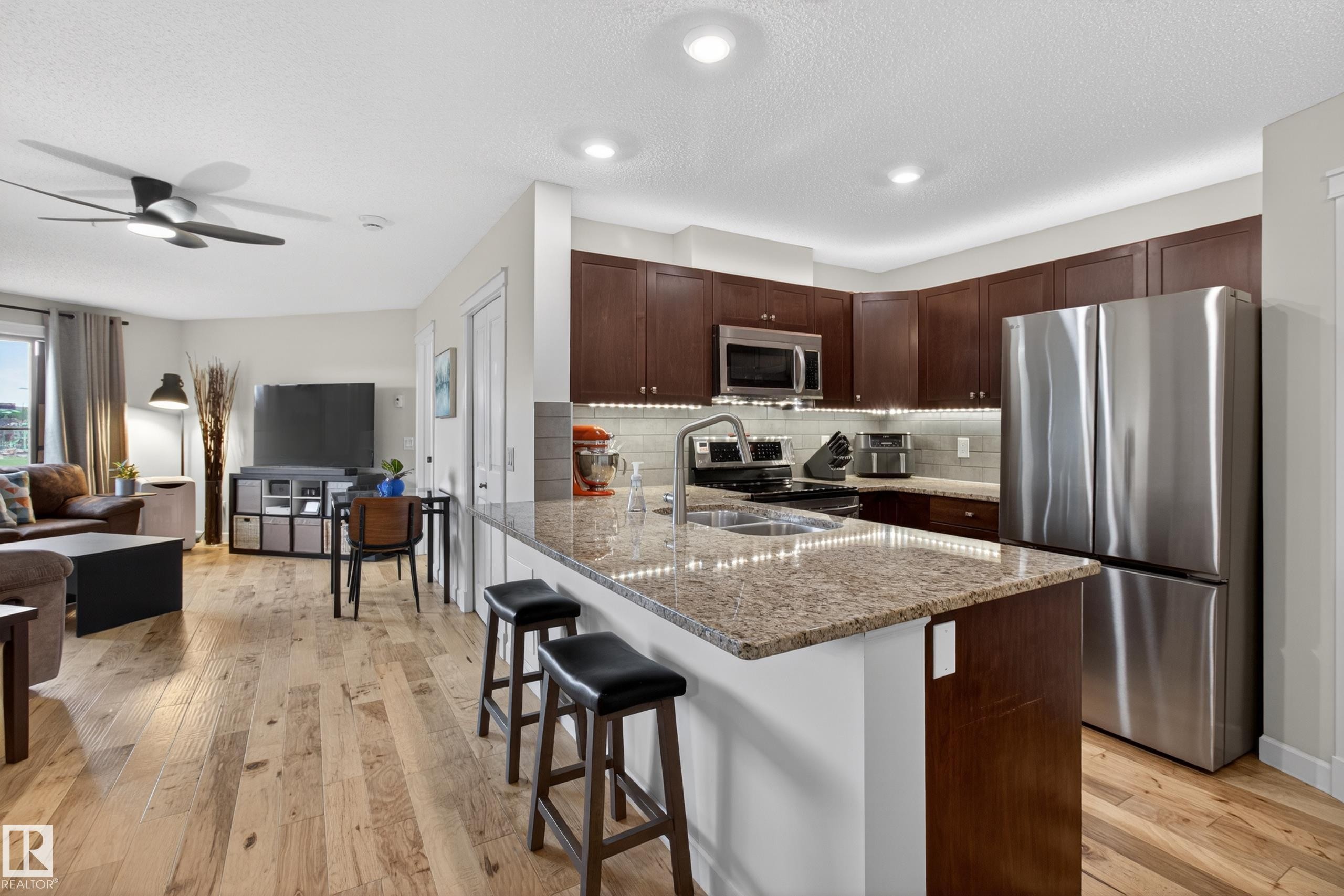 Gourmet kitchen with rich wood cabinetry, stainless steel appliances, and a spacious island featuring stone countertops and integrated sink - 211 3719 Whitelaw Lane, Edmonton, AB