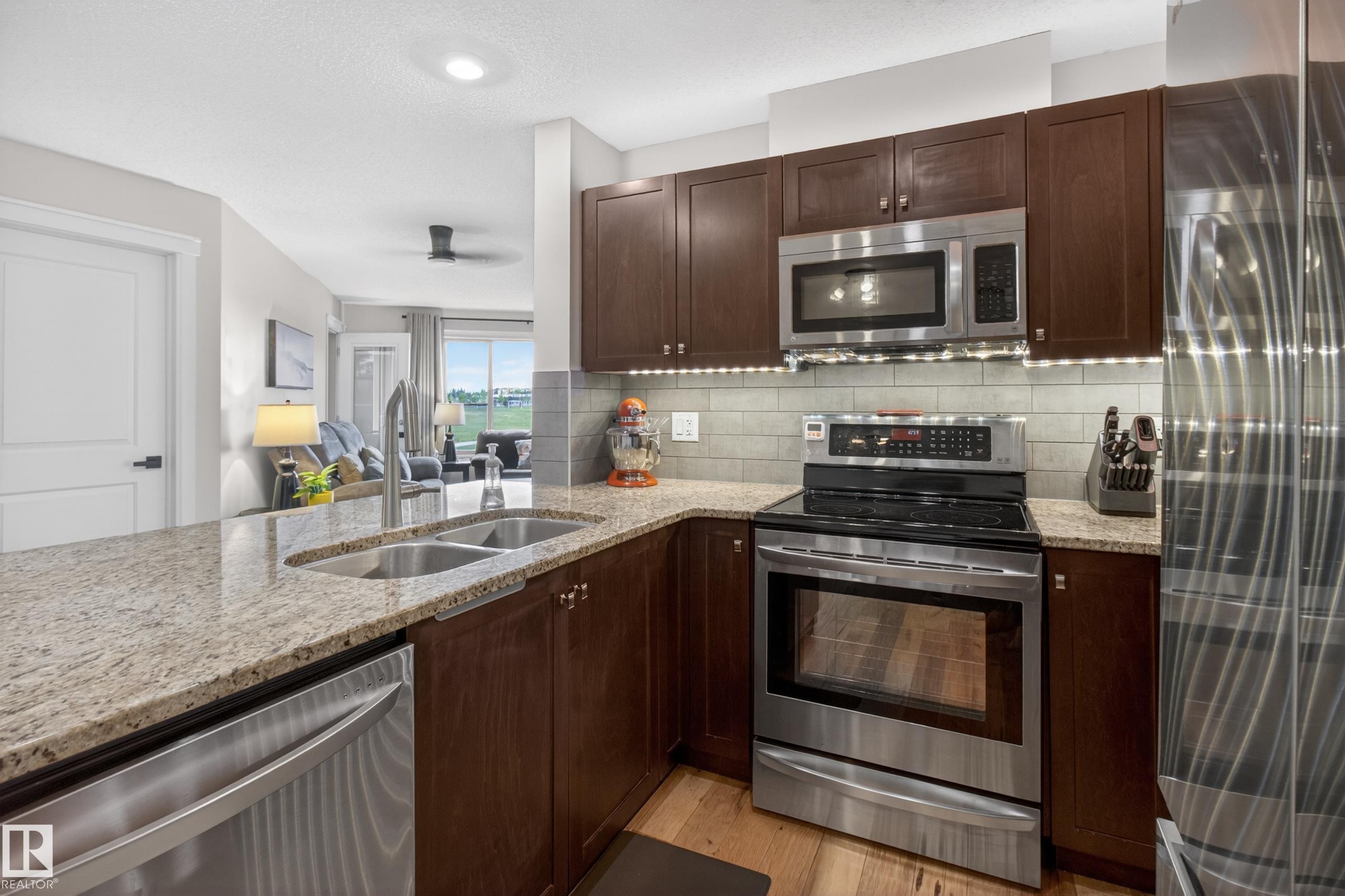 Kitchen featuring dark wood-finish cabinetry, light speckled countertops, and stainless steel appliances - 211 3719 Whitelaw Lane, Edmonton, AB