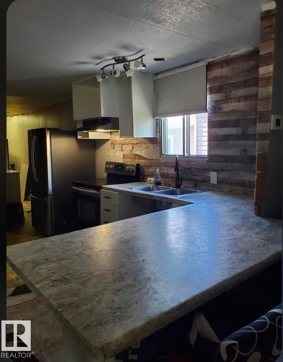 Kitchen featuring a U-shaped countertop, double basin sink, black appliances, track lighting, and wood plank wall accents - 14 Willowdale Drive, Edmonton, AB