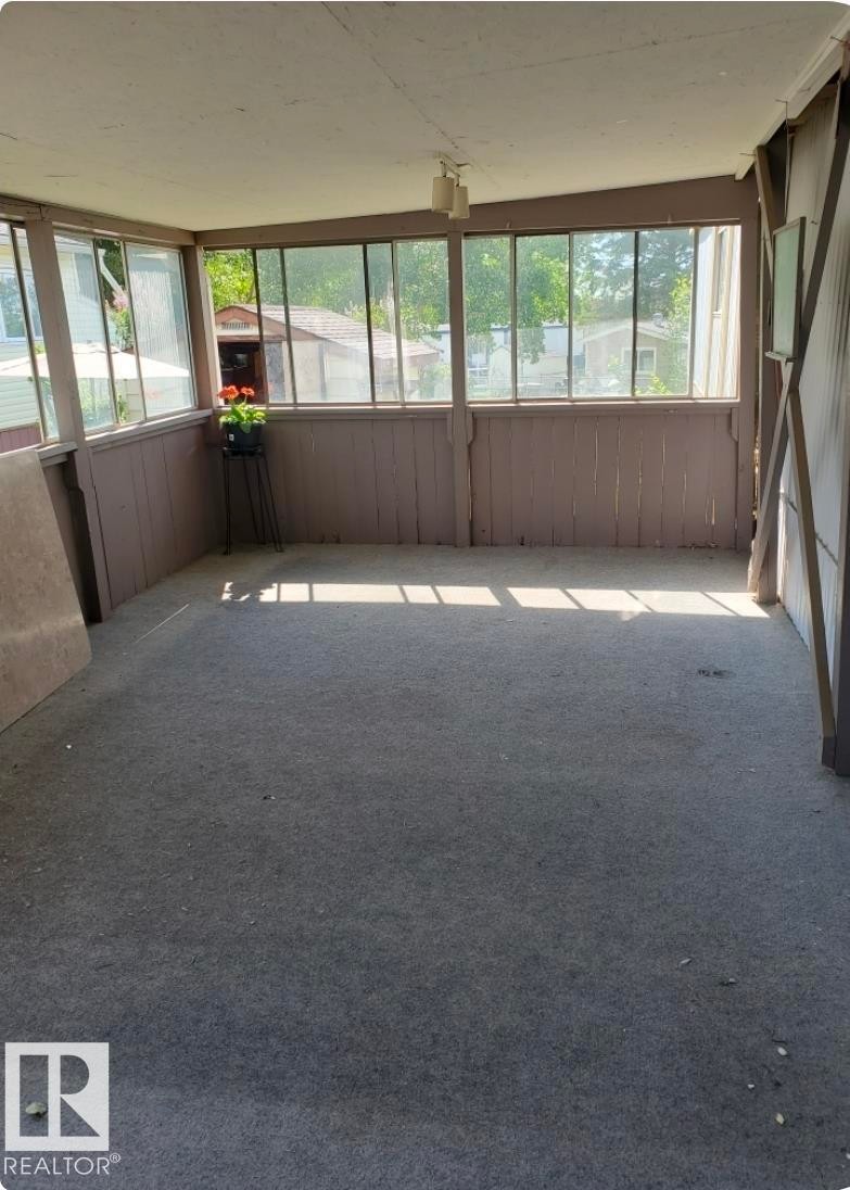 Enclosed sunroom featuring a paneled wood half-wall, multiple window panes, and a mounted ceiling light fixture - 14 Willowdale Drive, Edmonton, AB