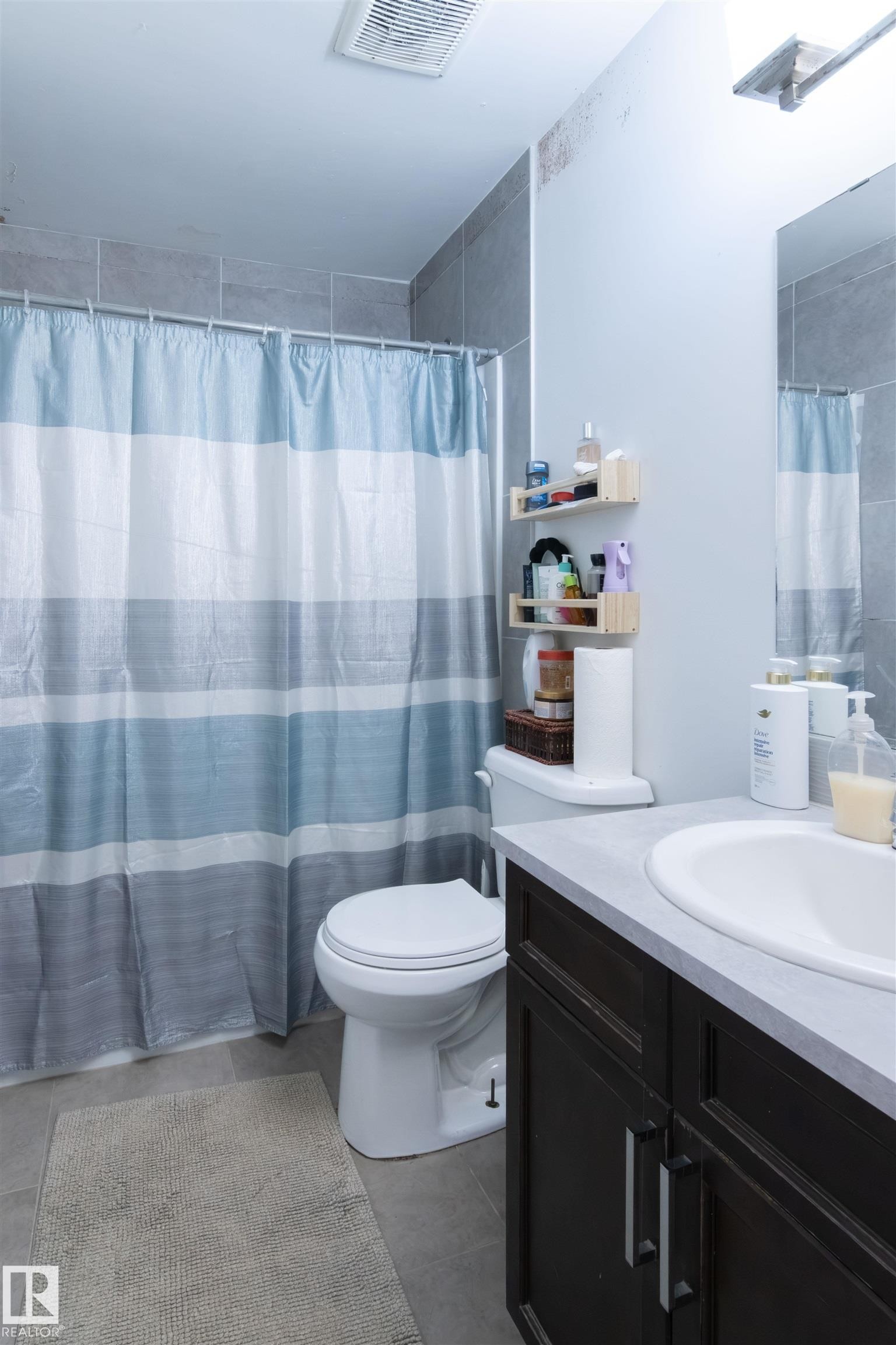 Bathroom featuring a toilet, a dark wood-finish vanity with a white countertop and integrated sink, and gray tiled flooring - 4004 88 Street Nw, Edmonton, AB - Indoor Photo Showing Bathroom