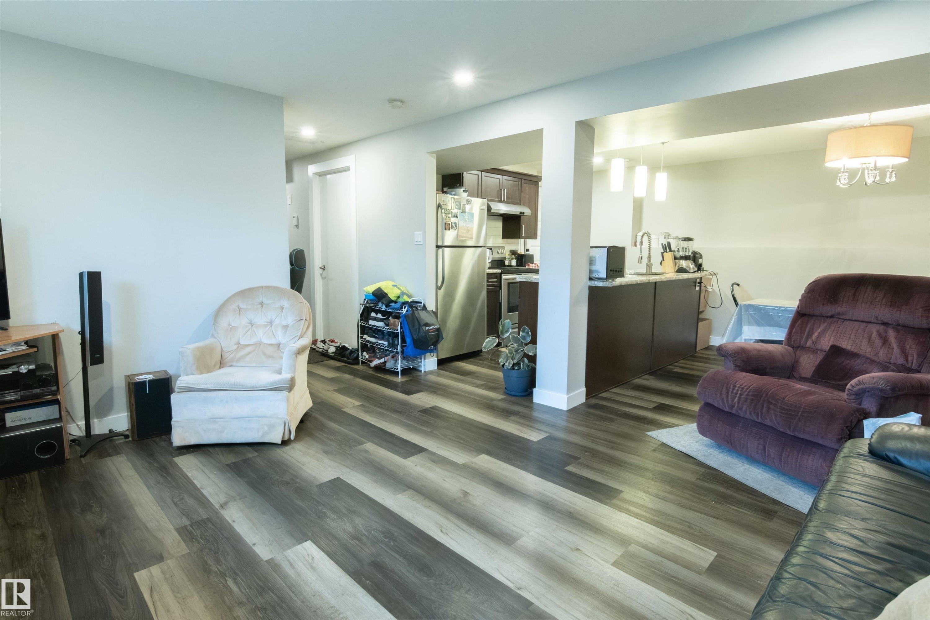Open-concept living area featuring wood-finish flooring, recessed lighting, and a kitchen with stainless steel appliances, dark cabinetry, and a peninsula with pendant lighting - 4004 88 Street Nw, Edmonton, AB - Indoor Photo Showing Living Room