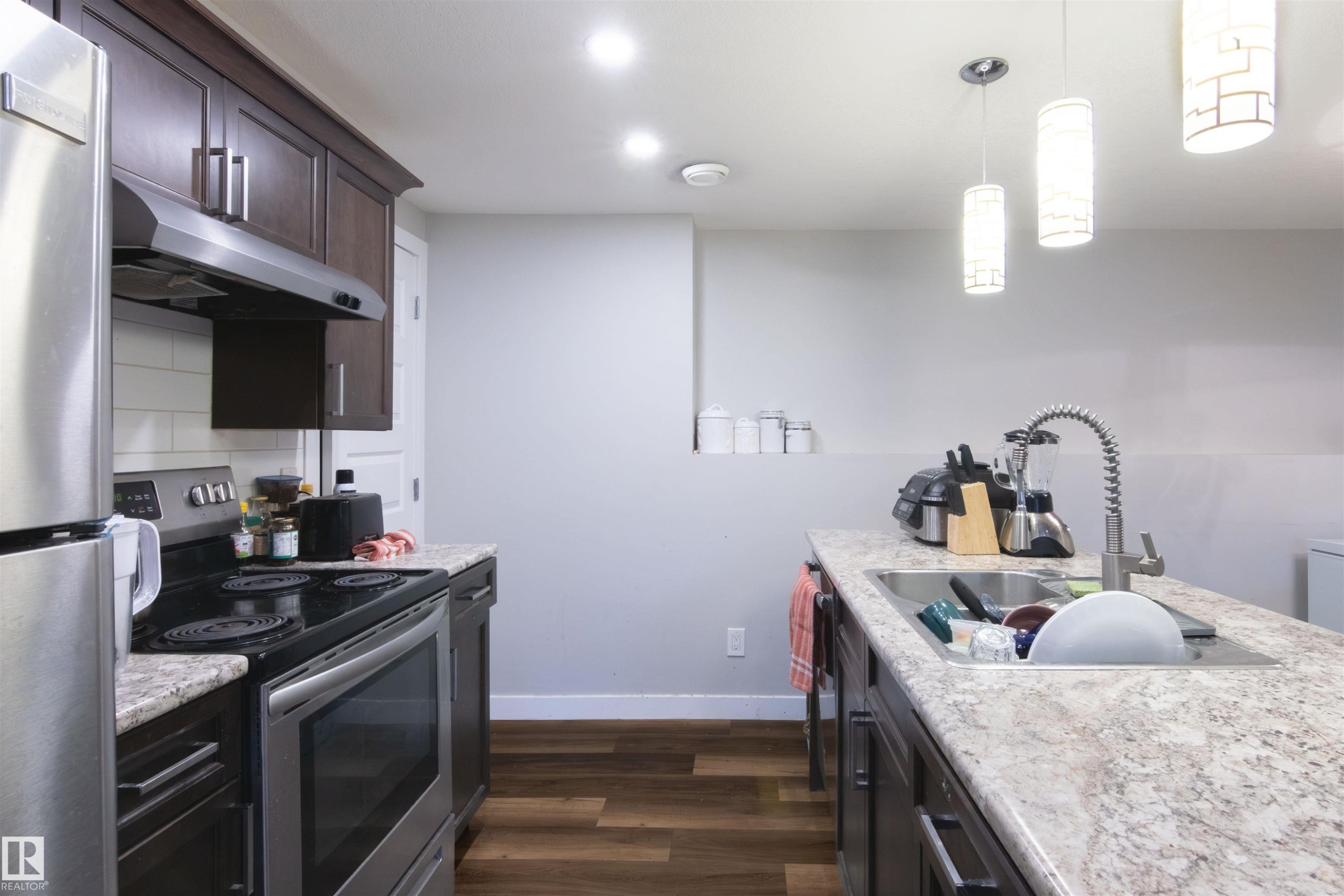 Contemporary kitchen featuring dark wood cabinetry, light-toned countertops, and stainless steel appliances - 4004 88 Street Nw, Edmonton, AB - Indoor Photo Showing Kitchen