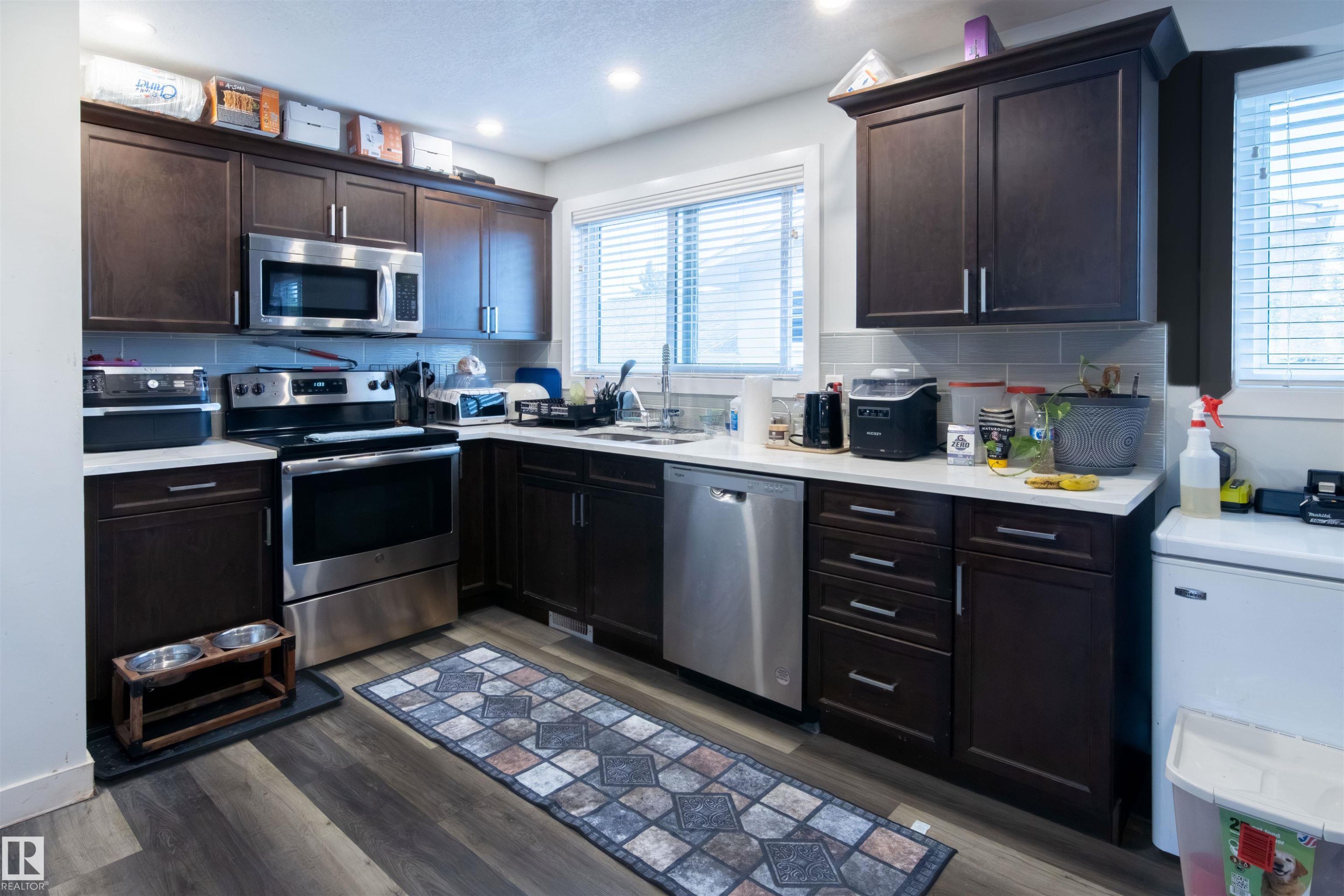 Kitchen featuring dark wood cabinetry, stainless steel appliances, light countertops, and a subway tile backsplash - 4004 88 Street Nw, Edmonton, AB - Indoor Photo Showing Kitchen