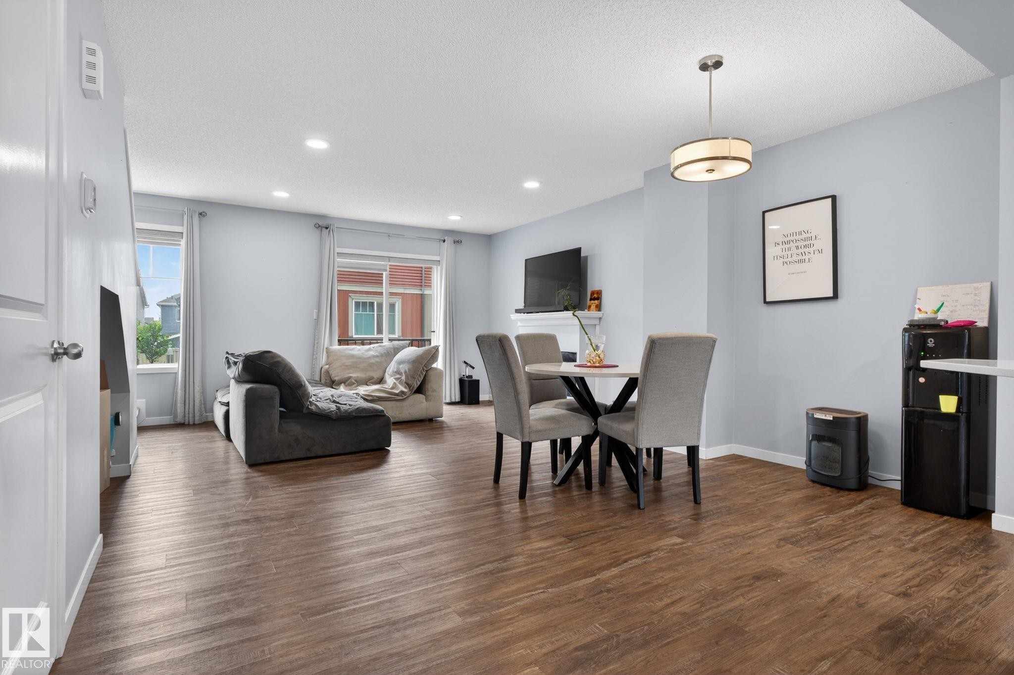 Open-concept living space with wood-finish flooring, recessed lighting, and ample natural light from multiple windows - 62 3305 Orchards Link, Edmonton, AB