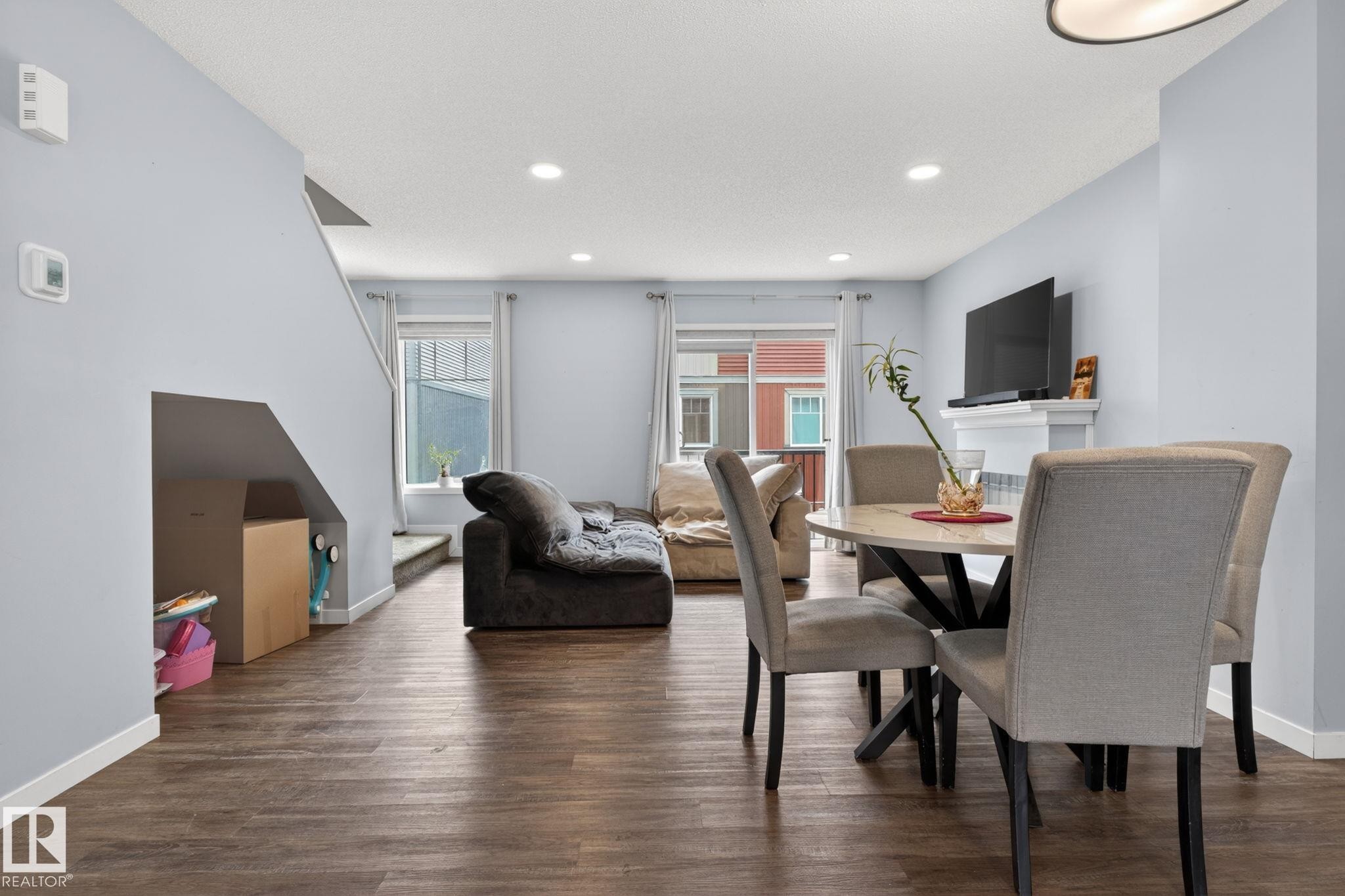 Open-concept living area featuring wood-finish flooring, recessed lighting, and a white fireplace mantel - 62 3305 Orchards Link, Edmonton, AB
