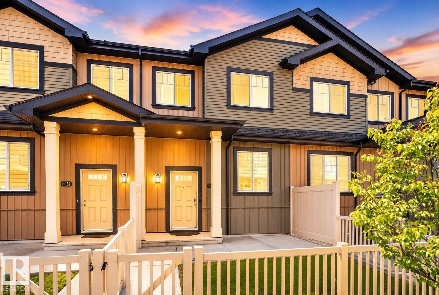 Multi-level townhome exterior featuring varied siding materials, dark trim, and a white picket fence - 62 3305 Orchards Link, Edmonton, AB