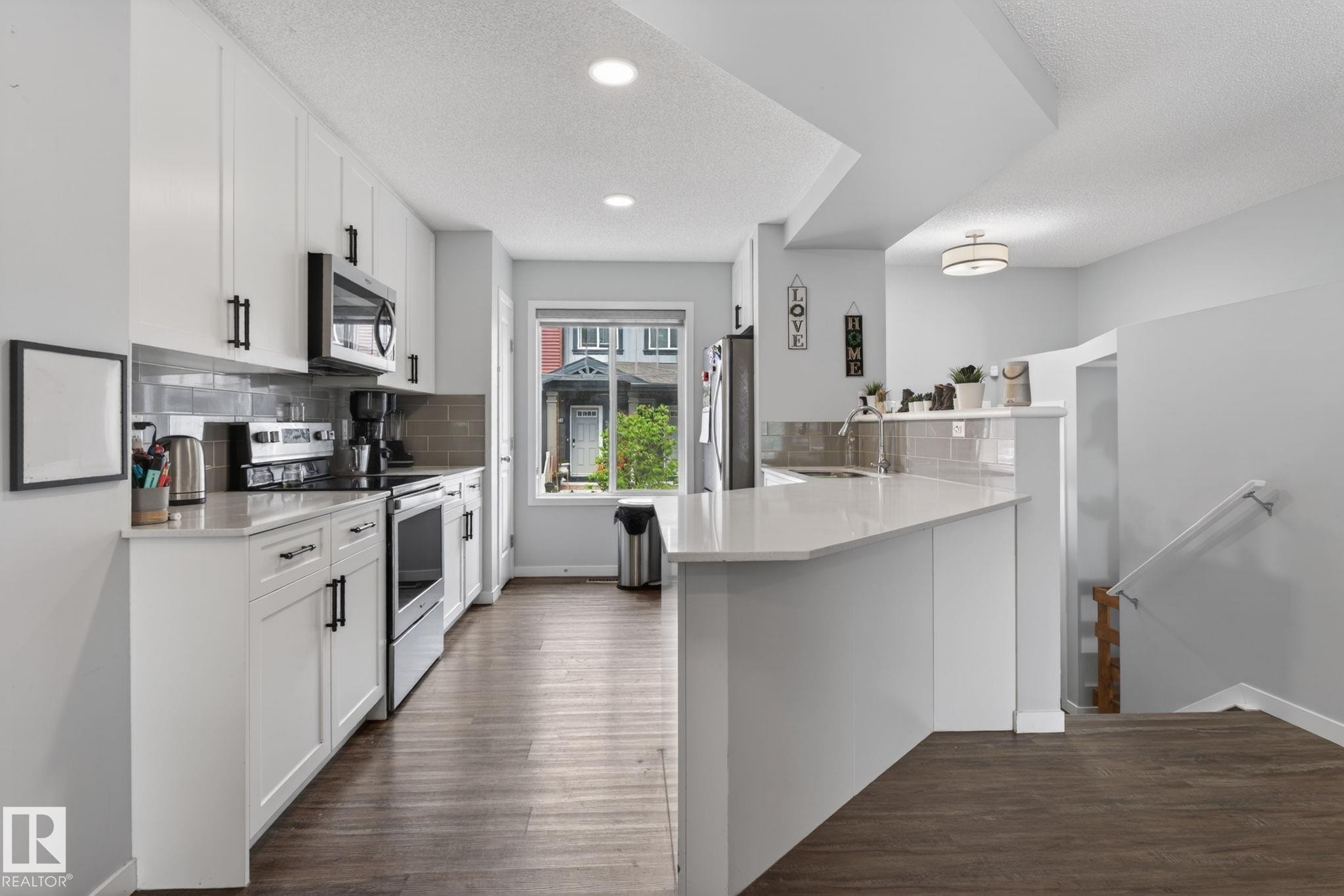 Modern kitchen featuring white cabinetry, stainless steel appliances, a tile backsplash, and light-toned countertops - 62 3305 Orchards Link, Edmonton, AB