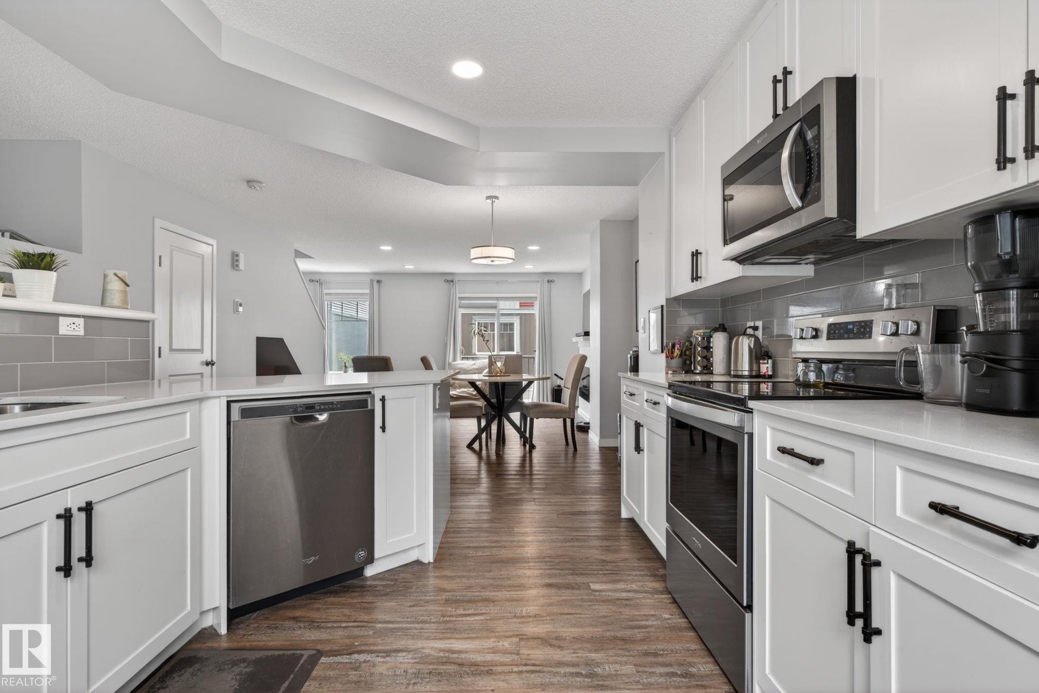 Well-appointed kitchen featuring white cabinetry, stainless steel appliances, light-toned countertops, and a gray subway tile backsplash - 62 3305 Orchards Link, Edmonton, AB