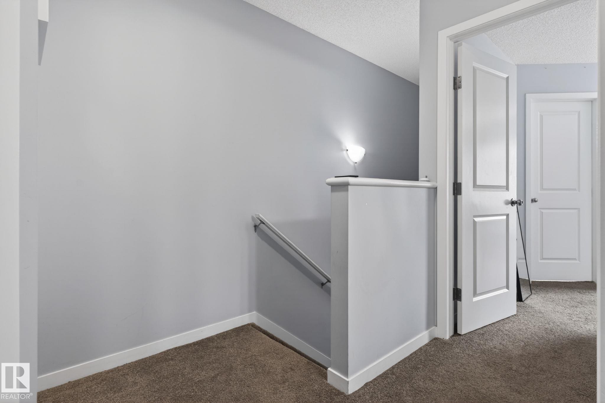 Carpeted hallway featuring light gray walls, white trim, and a white paneled door - 62 3305 Orchards Link, Edmonton, AB