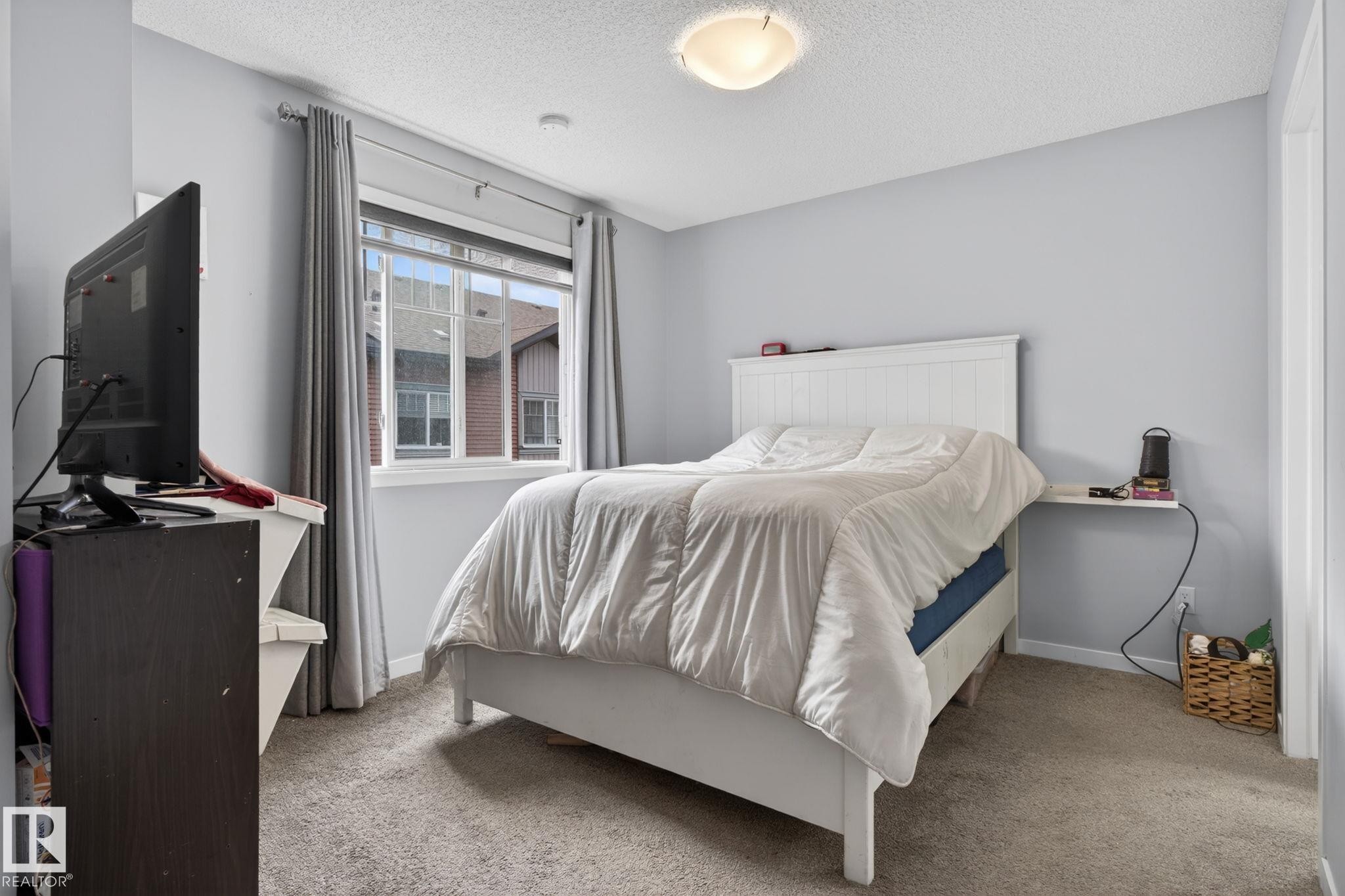 Carpeted bedroom with light blue walls and a window featuring white trim - 62 3305 Orchards Link, Edmonton, AB