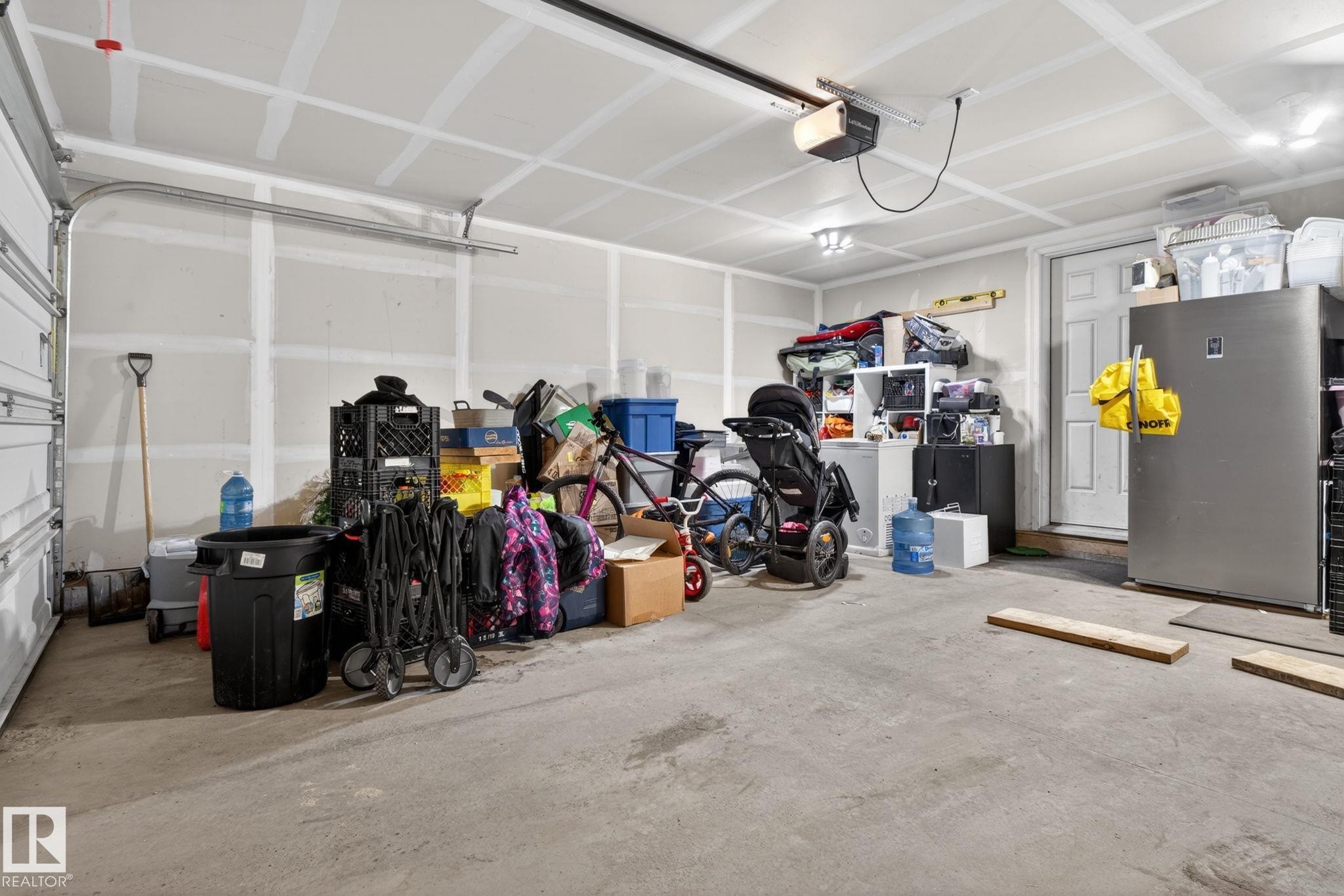Spacious garage featuring a concrete floor, painted drywall, overhead lighting, and an automatic garage door opener - 62 3305 Orchards Link, Edmonton, AB