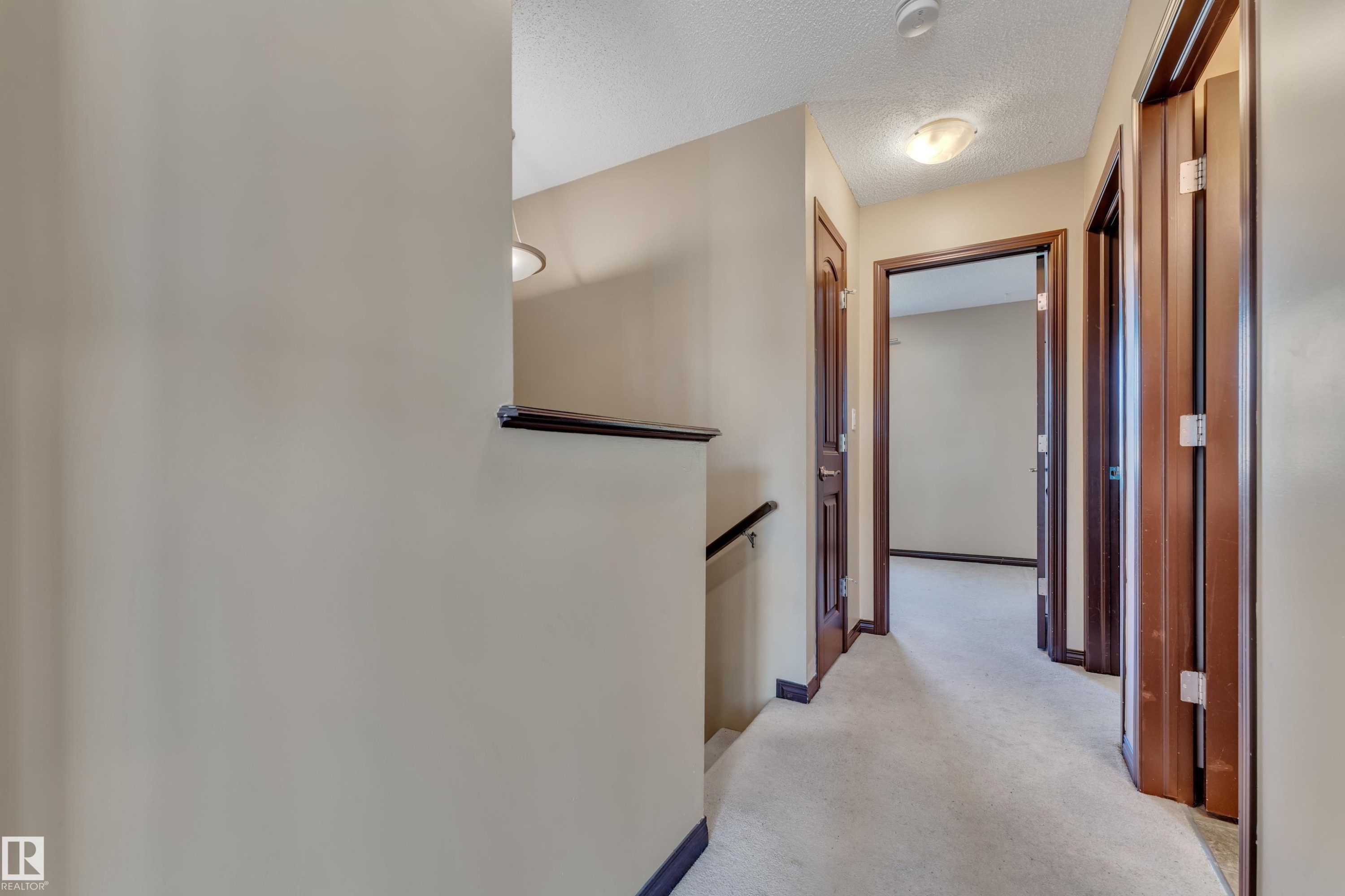 Hallway featuring light-toned wall paint, dark wood-finish doors, and plush carpet flooring - 621 Mcdonough Link Link, Edmonton, AB