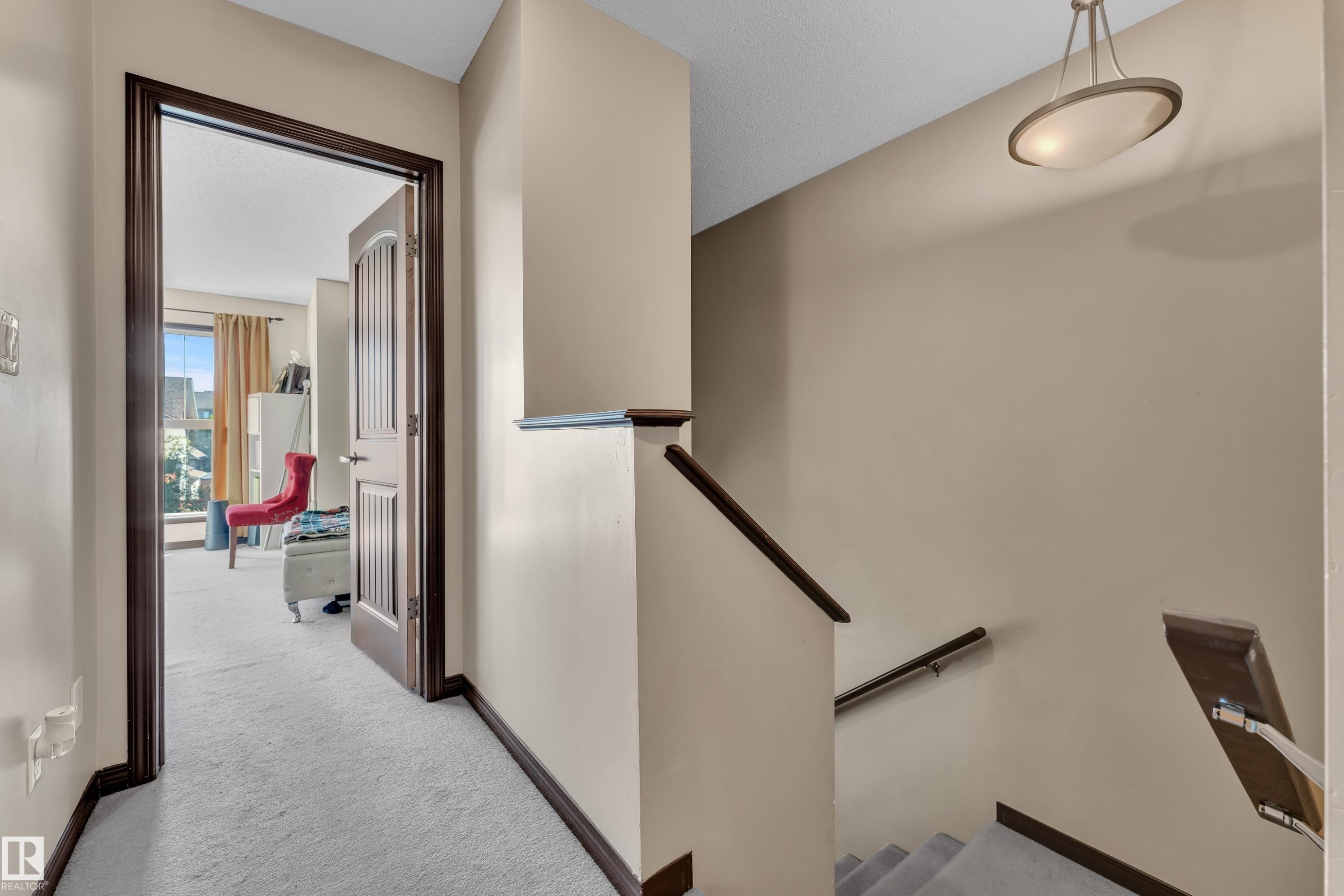 Carpeted hallway and staircase featuring dark wood trim, banister, and handrail - 621 Mcdonough Link Link, Edmonton, AB