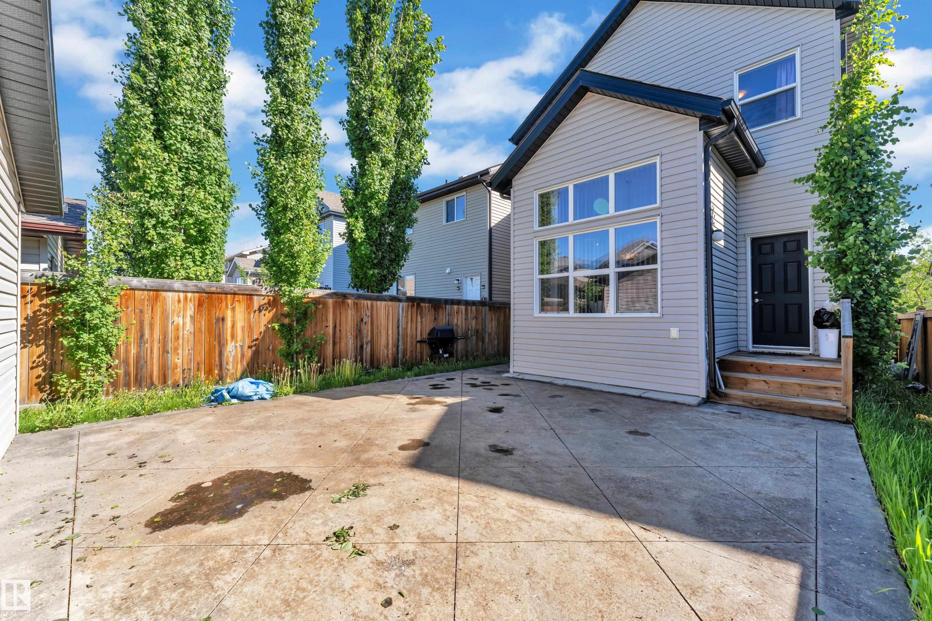 Rear exterior featuring light gray siding, multiple large windows, and a dark entry door with wood steps - 621 Mcdonough Link Link, Edmonton, AB