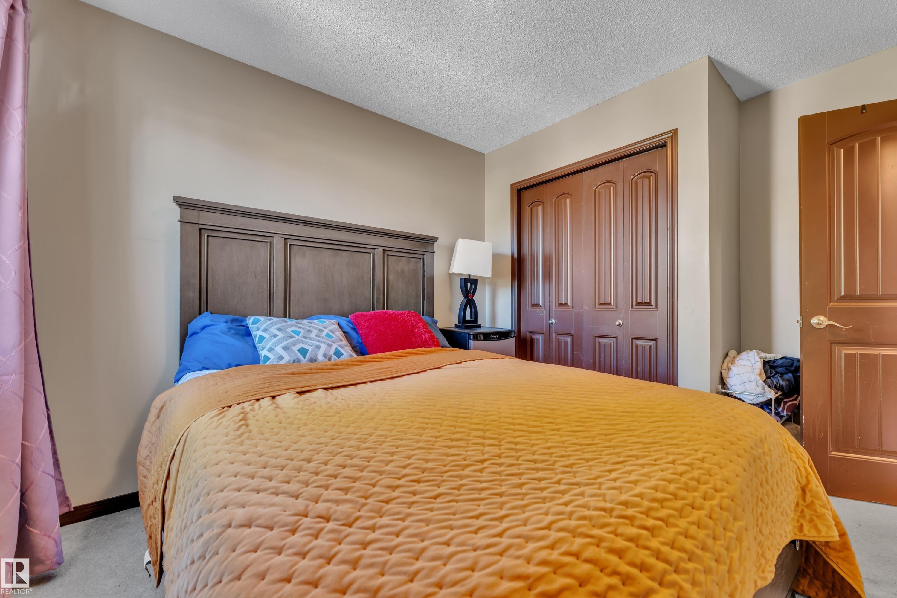 Inviting room featuring a paneled wood-finish headboard, bifold closet doors, a solid door with decorative paneling, and neutral wall paint - 621 Mcdonough Link Link, Edmonton, AB