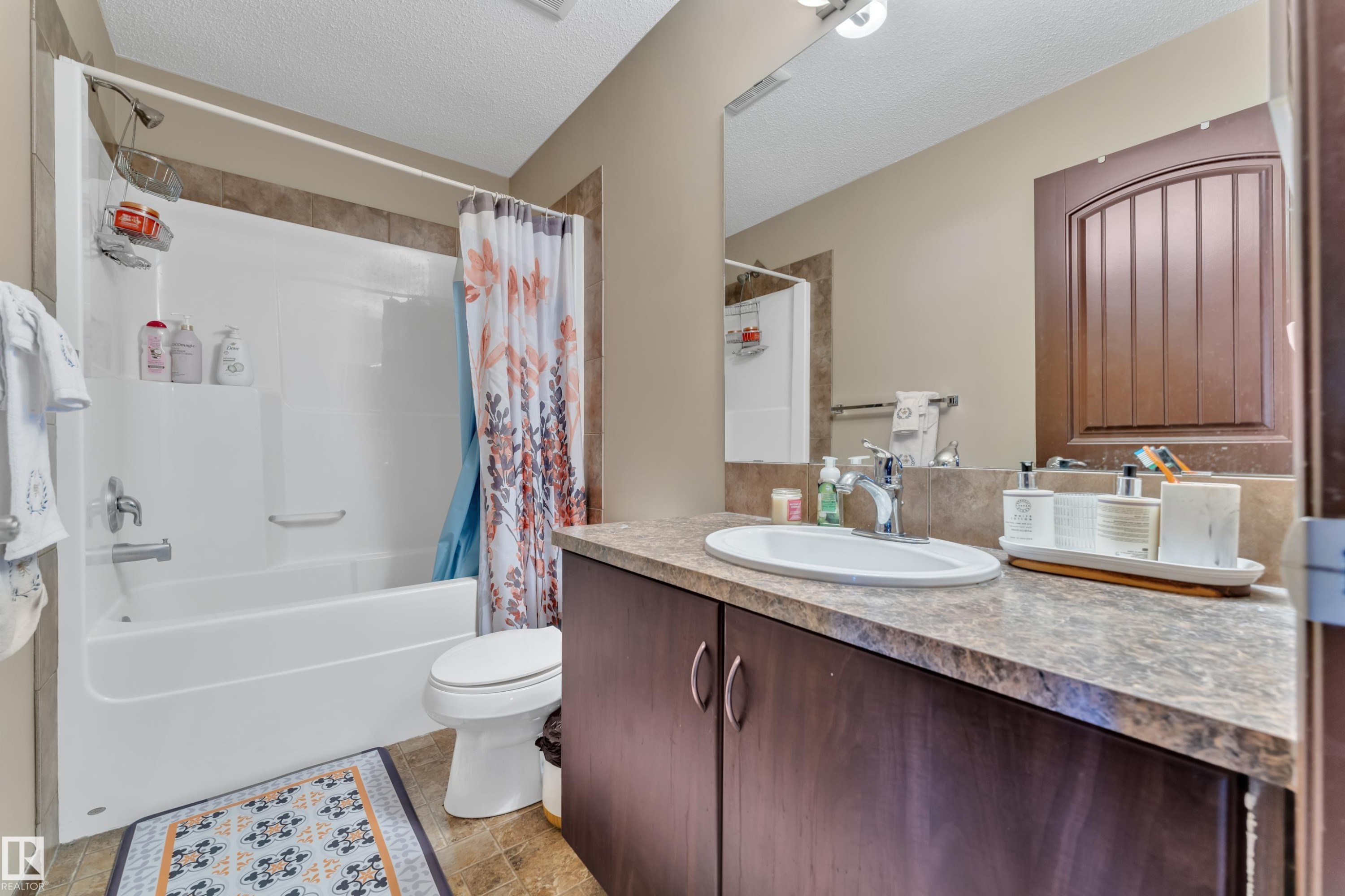 Full bathroom featuring a white tub and shower combination with tile surround, a dark wood-finish vanity, a spacious countertop, and an oval sink with a chrome faucet - 621 Mcdonough Link Link, Edmonton, AB