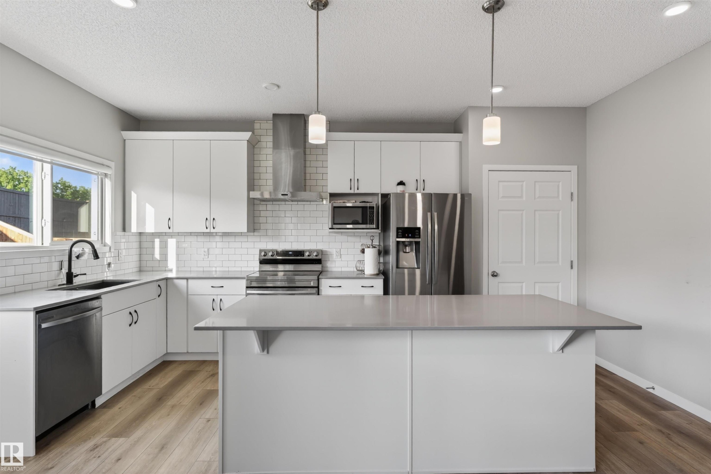 Contemporary kitchen featuring white cabinetry, subway tile backsplash, stainless steel appliances, a center island with countertop seating, and wood-finish flooring - 22638 99A Avenue, Edmonton, AB