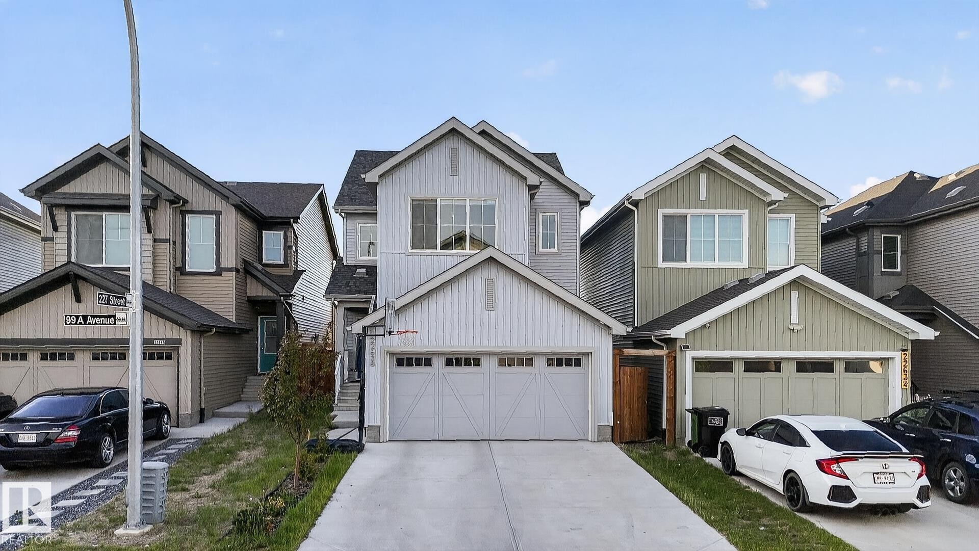Modern multi-story home featuring light gray vertical and horizontal siding, a two-car garage with a concrete driveway, and a gabled roofline - 22638 99A Avenue, Edmonton, AB