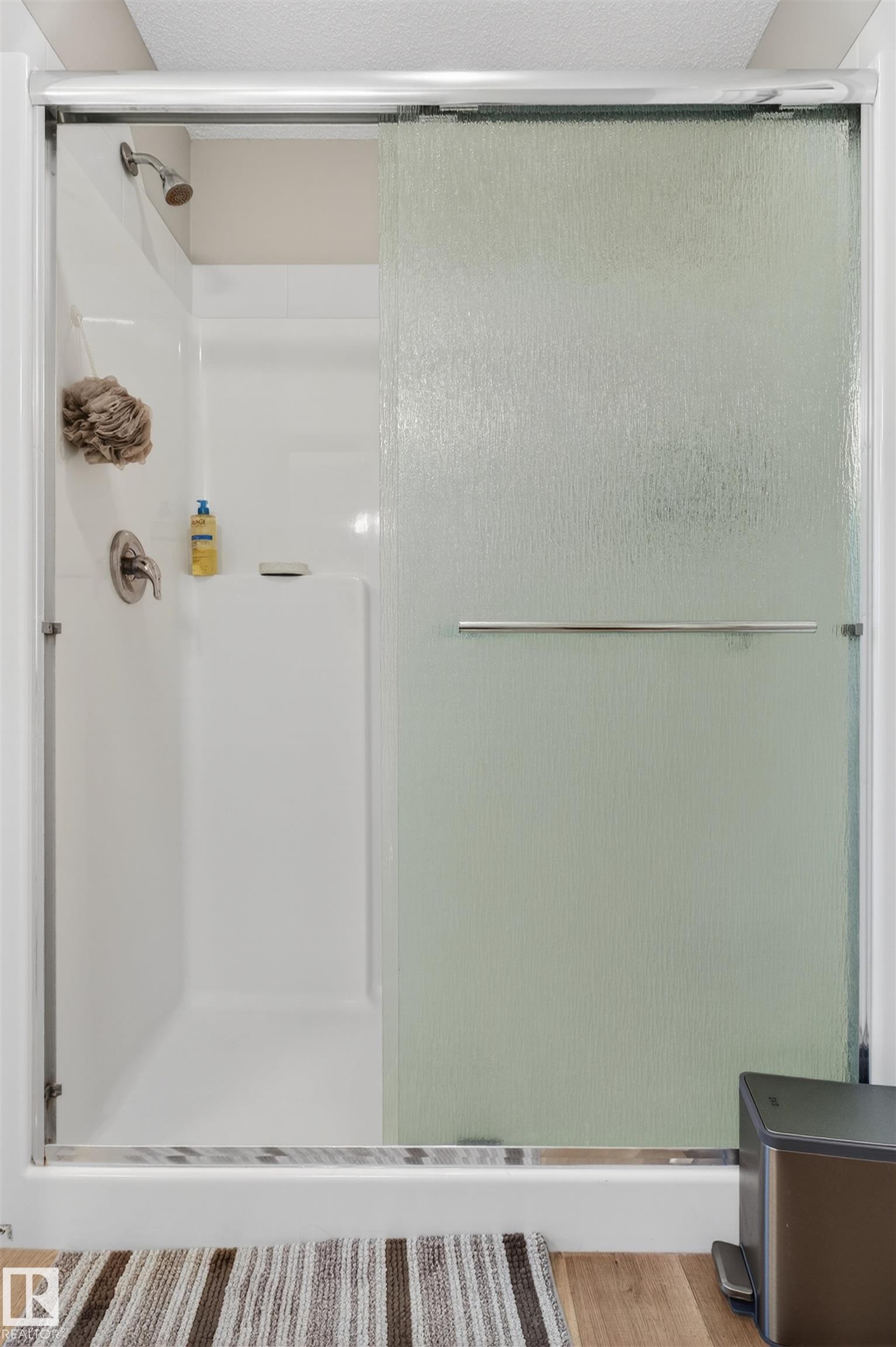 Shower enclosure featuring a sliding privacy glass door with a polished chrome handle, white multi-piece shower surround, and brushed nickel showerhead with coordinated fixtures - 22638 99A Avenue, Edmonton, AB