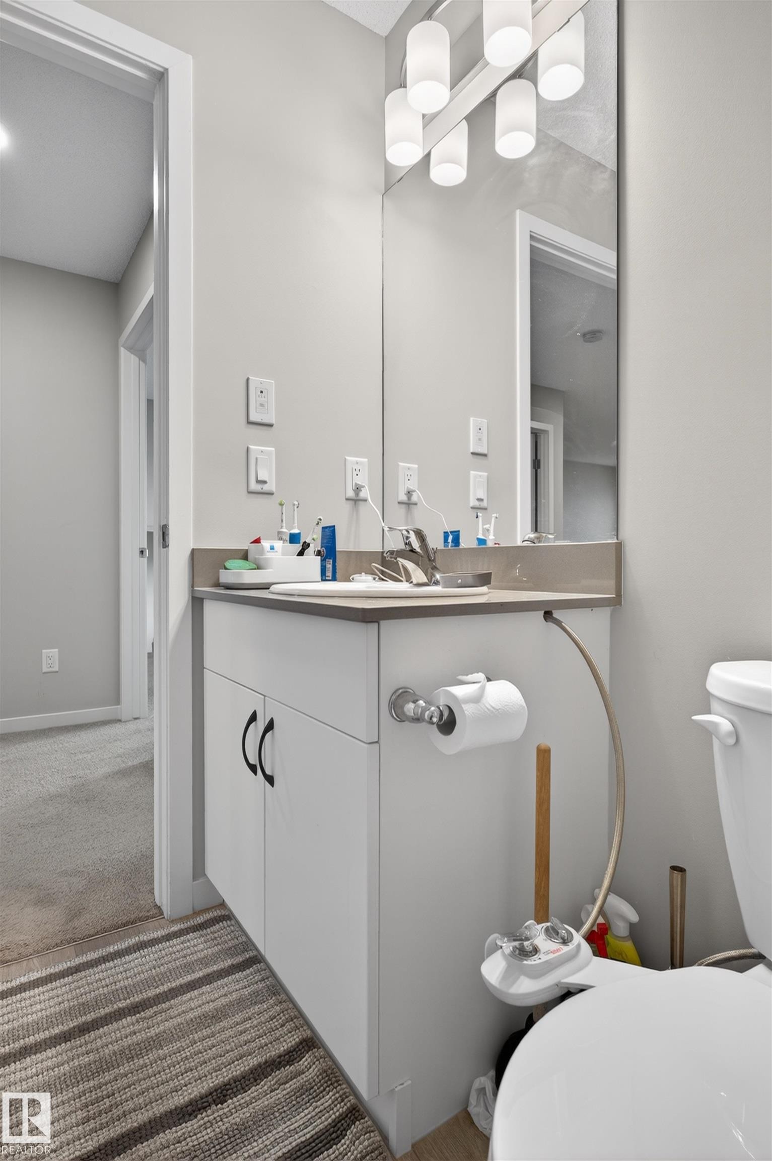 Bathroom vanity featuring white cabinetry with dark hardware, a light-toned countertop, and an integrated sink with a chrome faucet - 22638 99A Avenue, Edmonton, AB