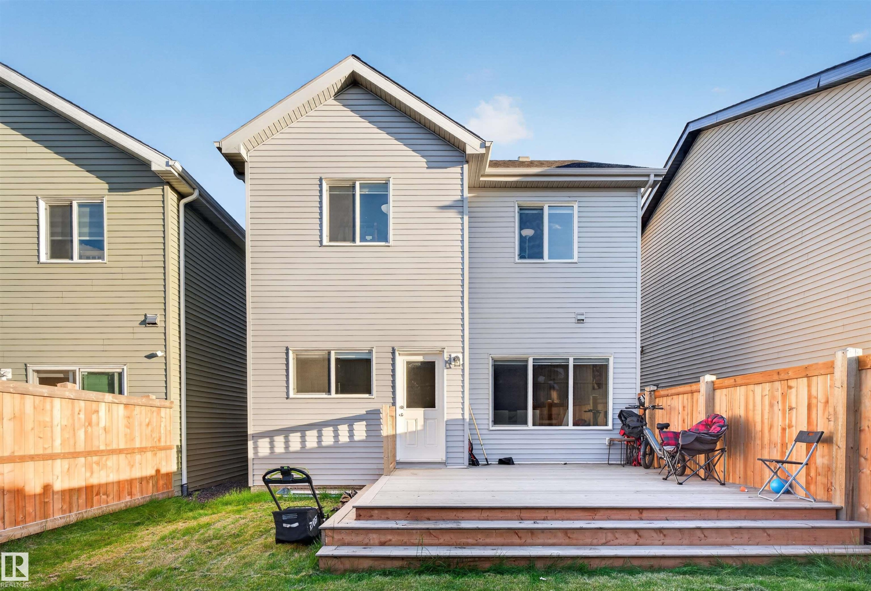 Rear exterior featuring light grey siding, a two-tier wood deck, and a fenced yard with natural grass - 22638 99A Avenue, Edmonton, AB