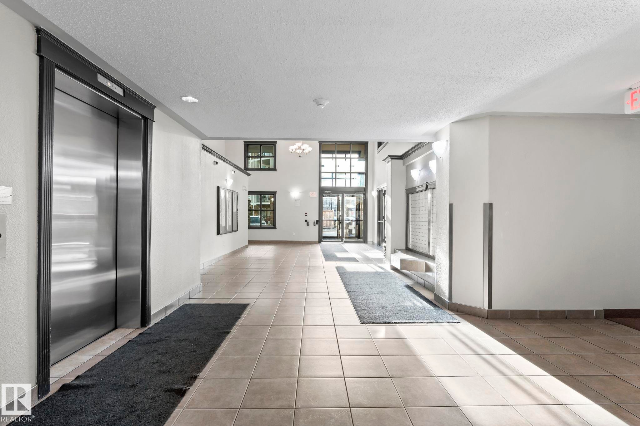Building entryway featuring a stainless steel elevator, light-toned tile flooring, and large windows at the main entrance - 2106 9357 Simpson Dr Nw, Edmonton, AB - Indoor Photo Showing Other Room