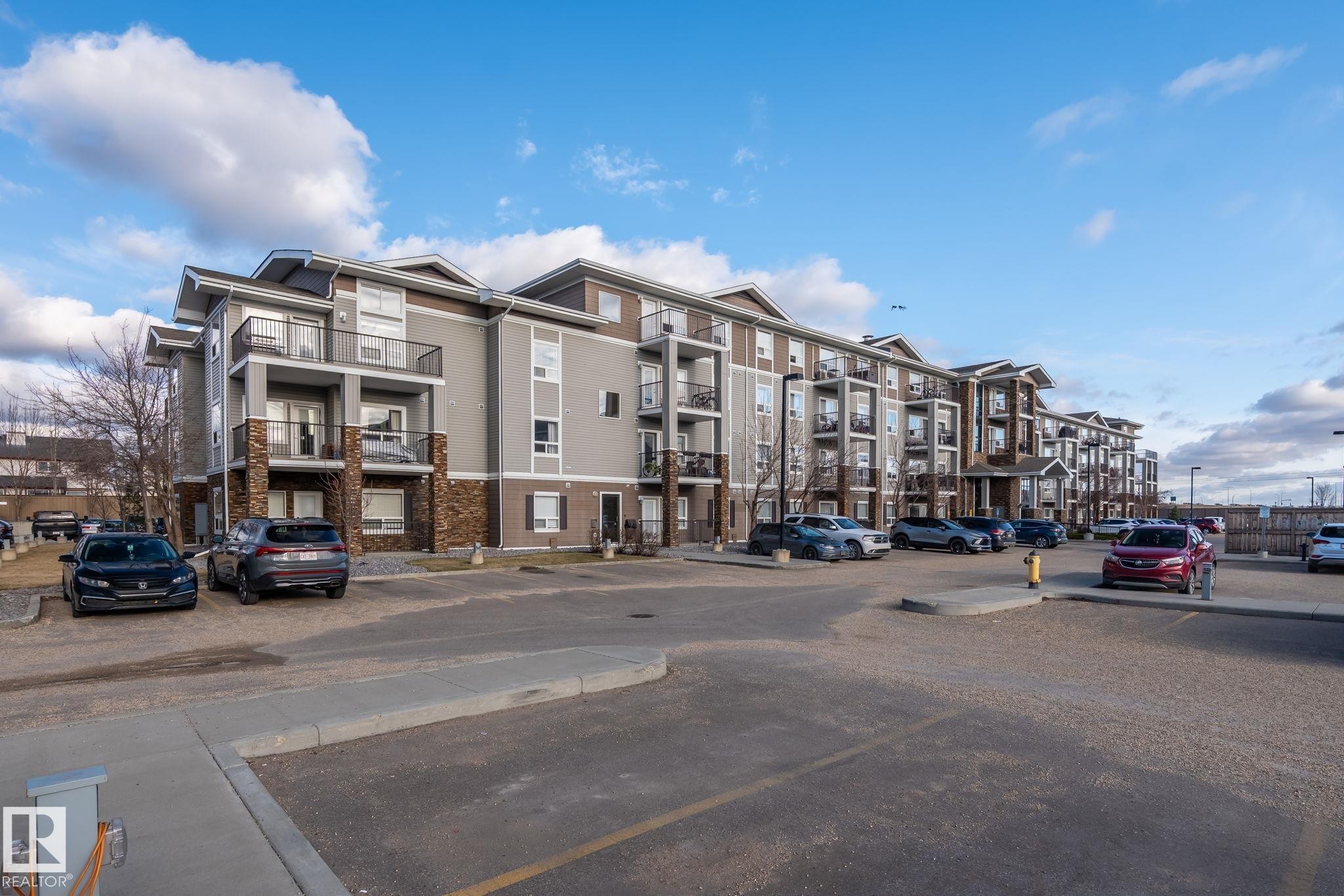 Multi-story residential building featuring balconies with black railings, stone veneer accents, and a large paved parking area - 2106 9357 Simpson Dr Nw, Edmonton, AB - Outdoor With Facade