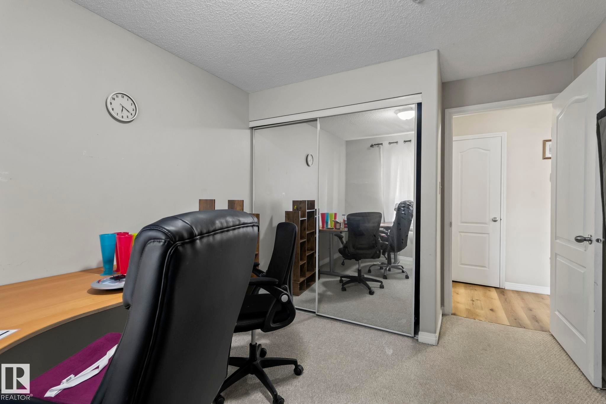 Carpeted interior room featuring mirrored closet doors, a white paneled door, and light-colored walls - 2106 9357 Simpson Dr Nw, Edmonton, AB - Indoor Photo Showing Office