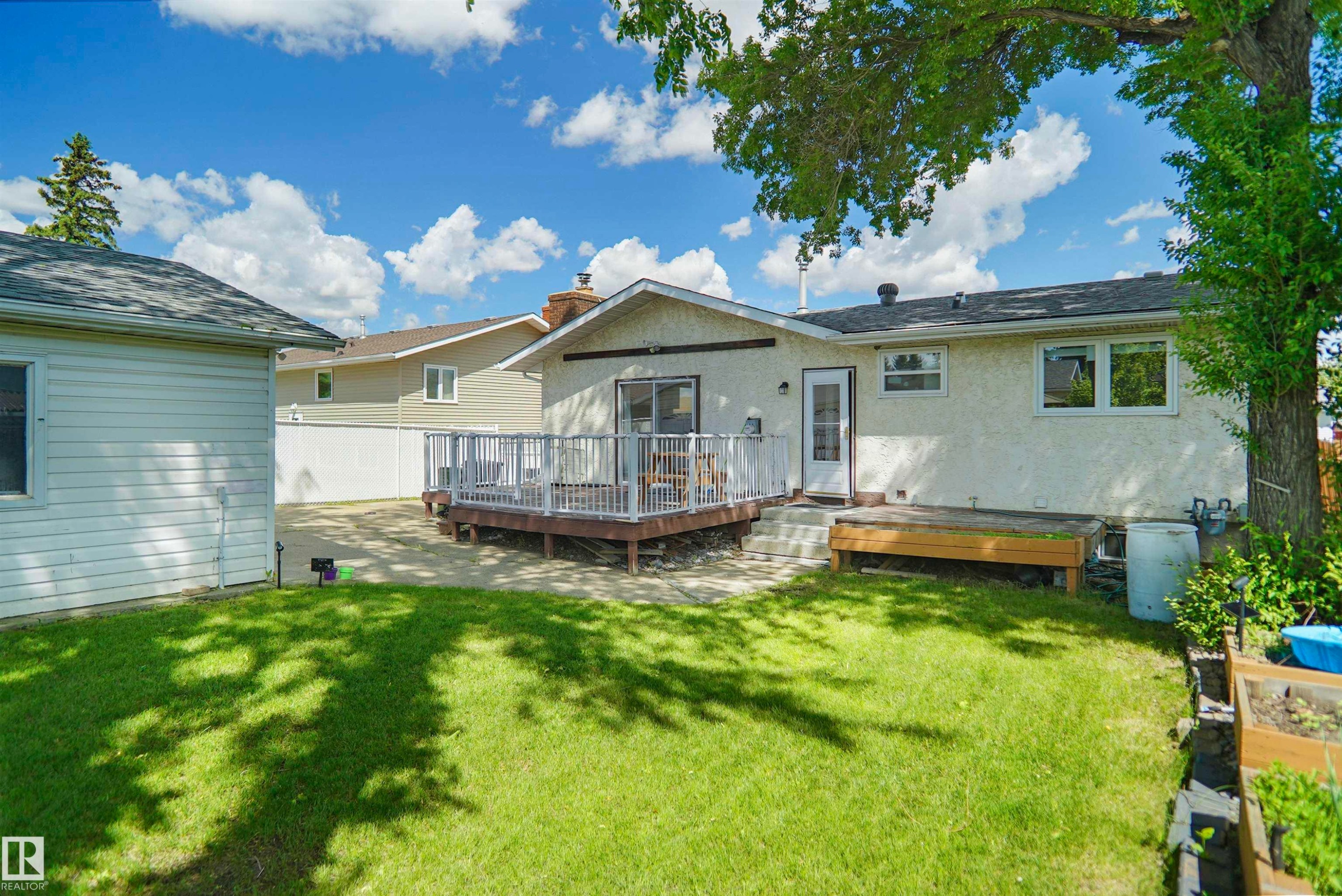 Expansive backyard featuring a manicured lawn, a multi-level wood deck with white railings, a detached garage with siding, and a wooden raised garden bed - 13524 26 Street, Edmonton, AB