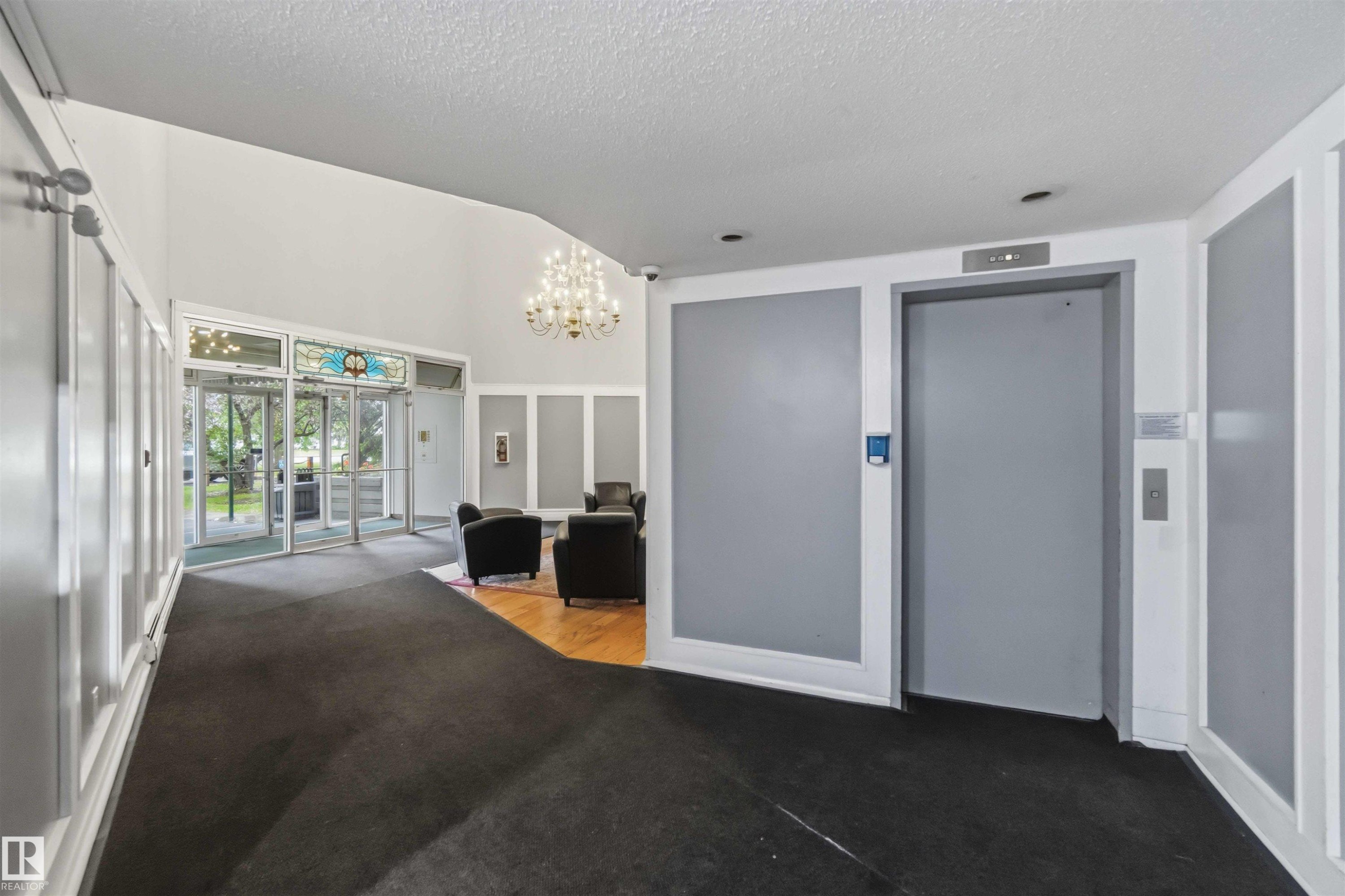 Lobby area featuring dual glass entry doors with a decorative transom, a prominent chandelier, recessed lighting, and a passenger elevator - #121 5125 Riverbend Rd Nw Nw, Edmonton, AB - Indoor Photo Showing Other Room