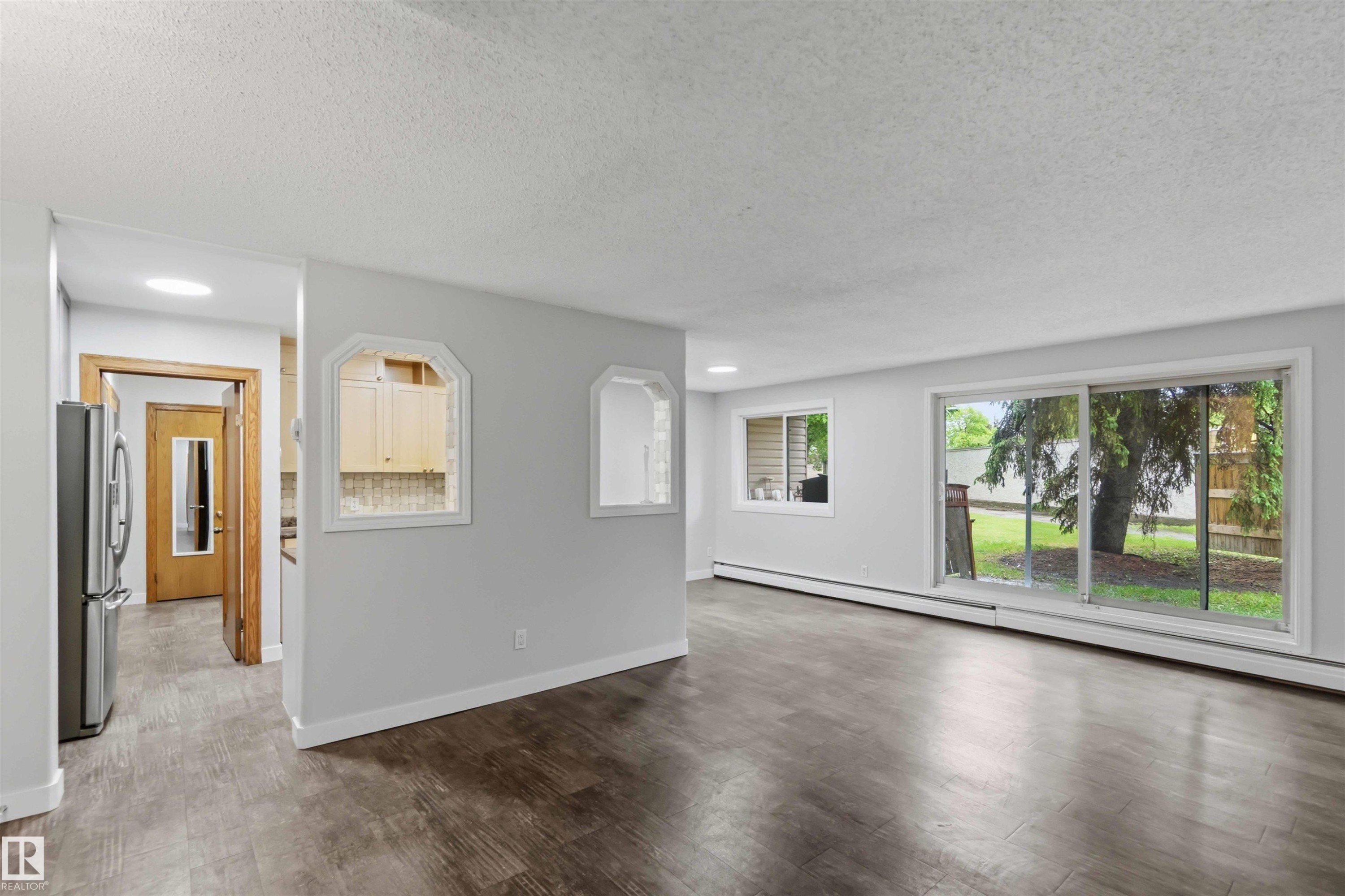 Spacious room featuring wood-finish flooring, light grey wall paint, and white baseboards - #121 5125 Riverbend Rd Nw Nw, Edmonton, AB - Indoor