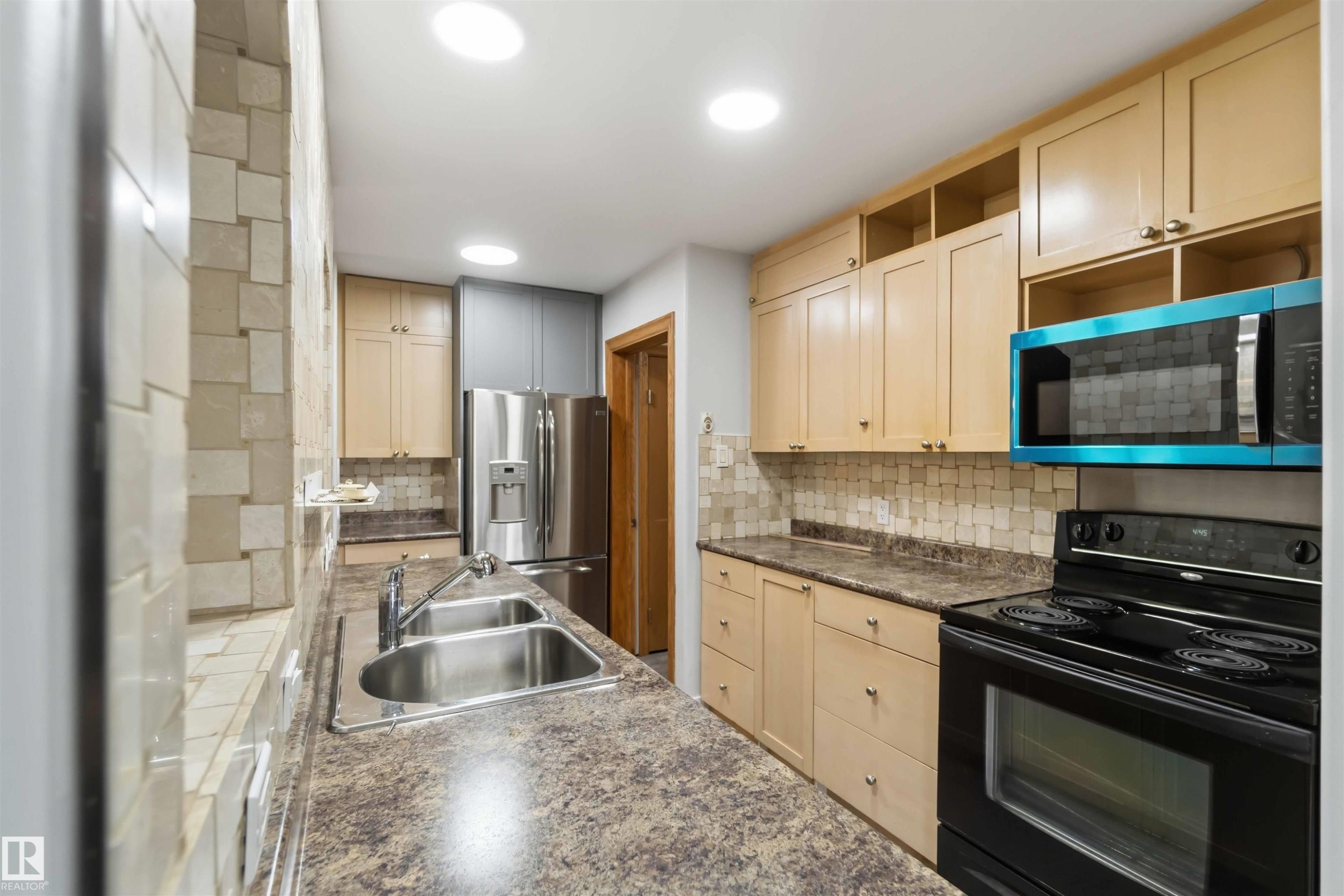 Modern kitchen featuring light wood cabinetry, a double basin stainless steel sink, a stainless steel French door refrigerator, and a black electric range - #121 5125 Riverbend Rd Nw Nw, Edmonton, AB - Indoor Photo Showing Kitchen With Double Sink