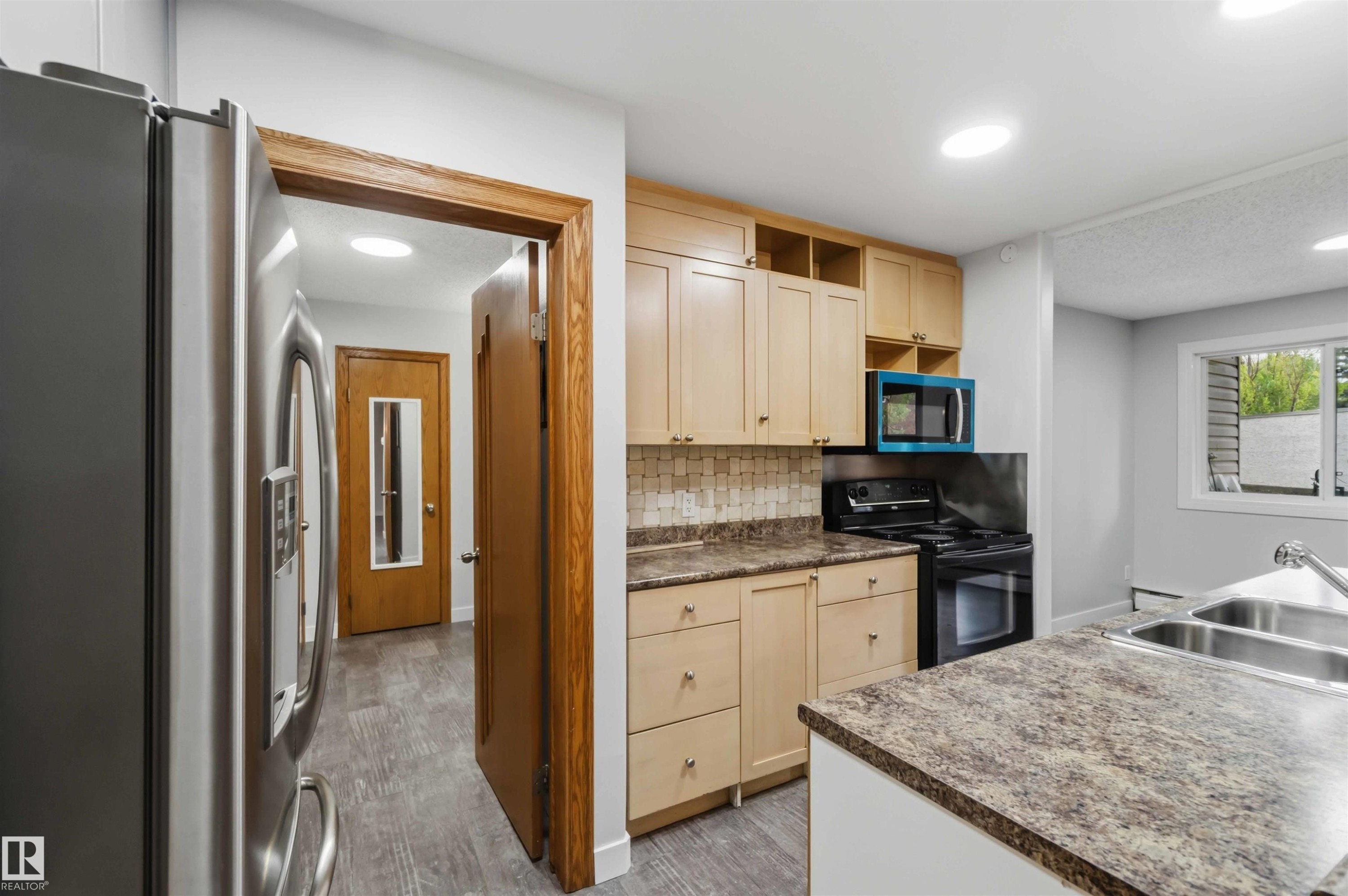 Kitchen featuring light wood-finish cabinetry, patterned countertops, and a tiled backsplash - #121 5125 Riverbend Rd Nw Nw, Edmonton, AB - Indoor Photo Showing Kitchen With Double Sink