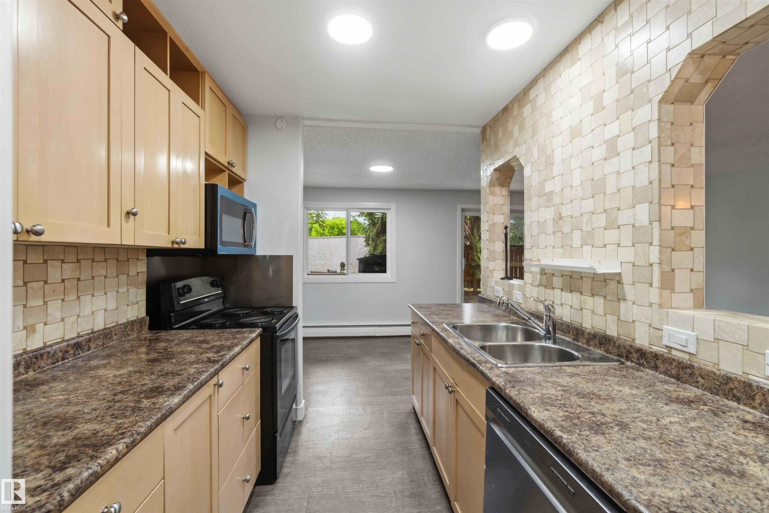 Kitchen with light wood-finish cabinetry, dark speckled countertops, and a full tile backsplash - #121 5125 Riverbend Rd Nw Nw, Edmonton, AB - Indoor Photo Showing Kitchen With Double Sink