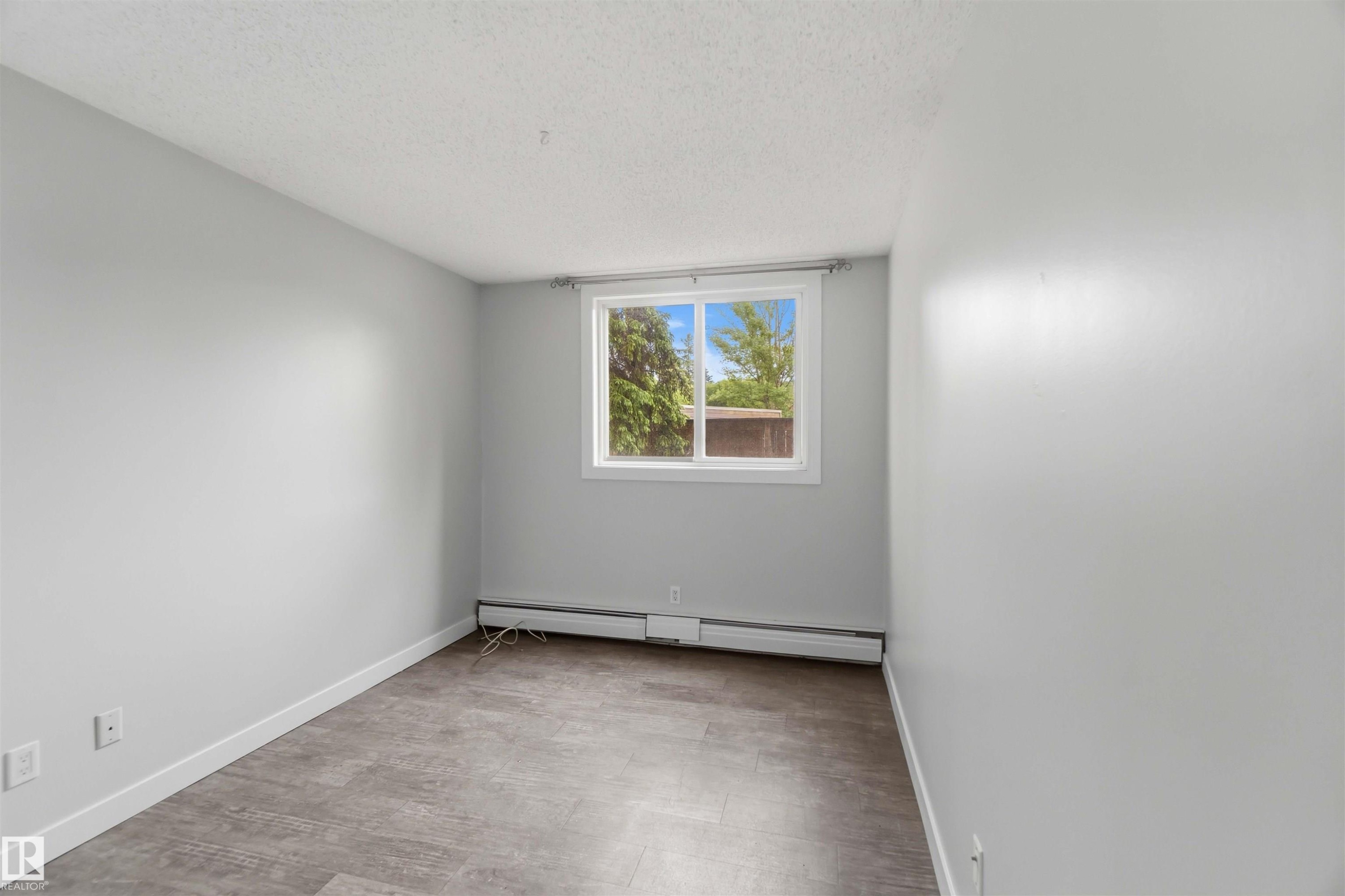 Neutral wall paint, wood-finish flooring, white trim, and a window with a white frame - #121 5125 Riverbend Rd Nw Nw, Edmonton, AB - Indoor Photo Showing Other Room