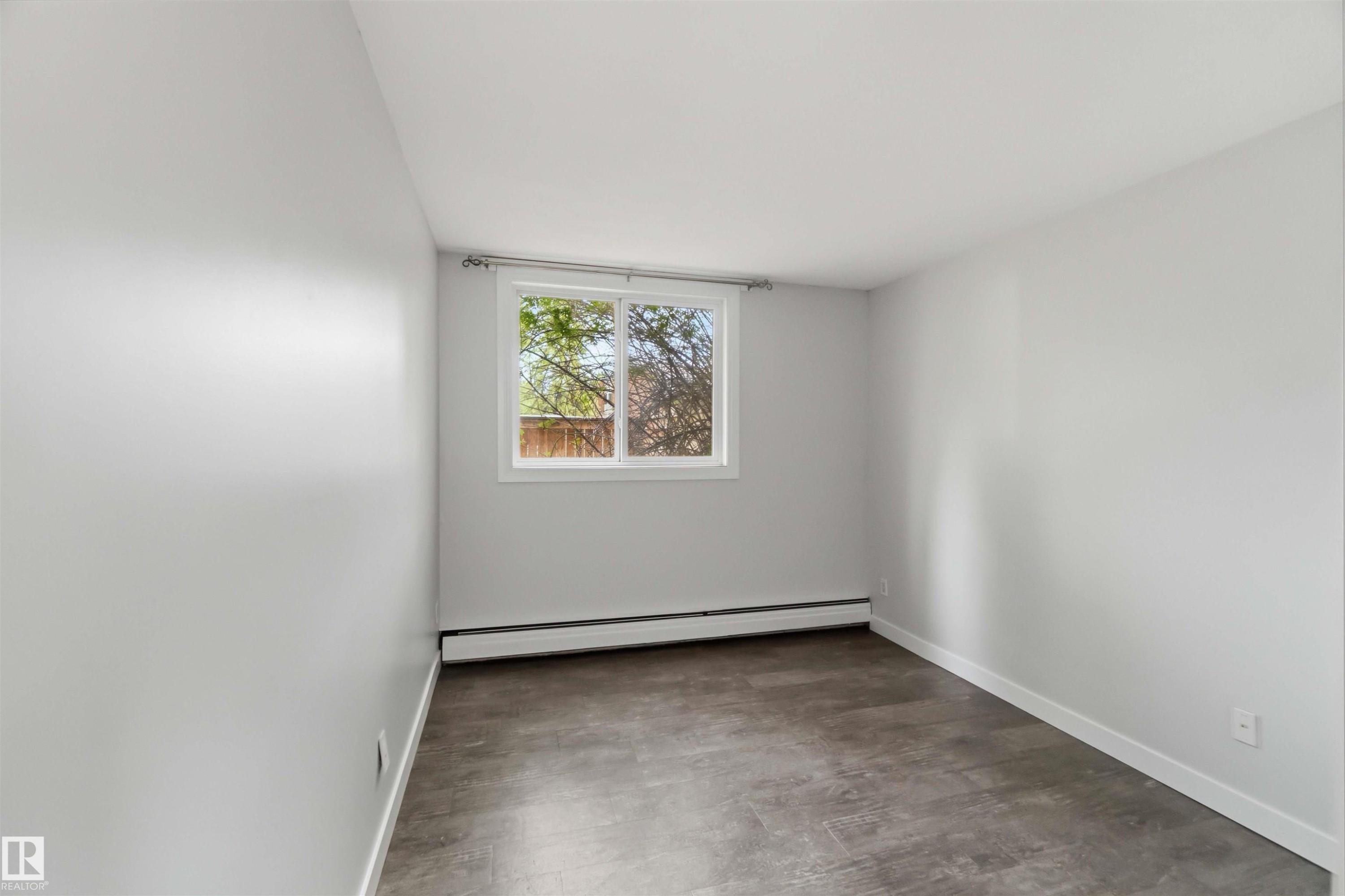 Windowed room featuring light gray walls, dark wood-finish flooring, and white baseboards - #121 5125 Riverbend Rd Nw Nw, Edmonton, AB - Indoor Photo Showing Other Room