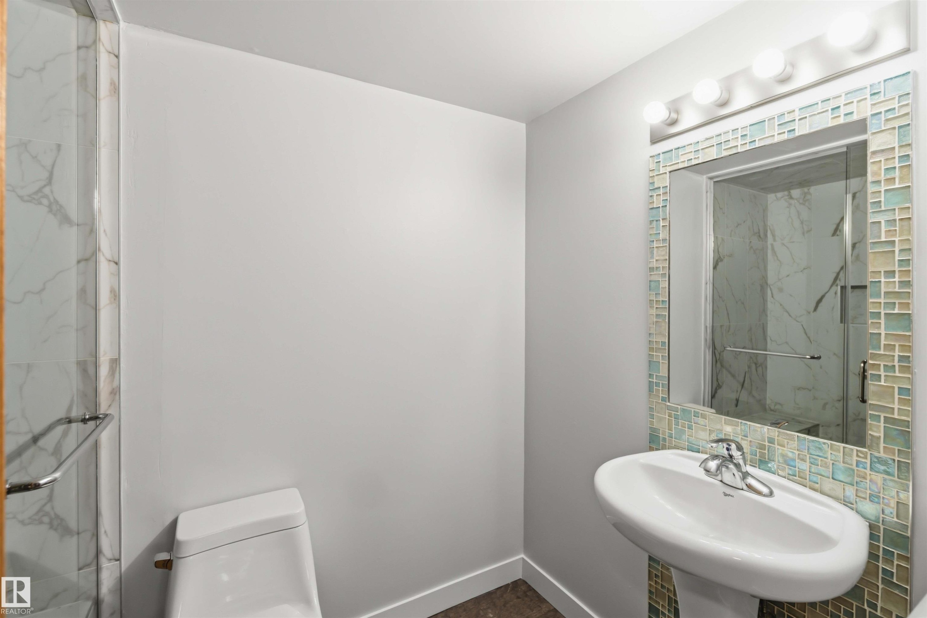 Modern bathroom featuring a tiled mirror frame, pedestal sink, and glass-enclosed shower with marble-look tile - #121 5125 Riverbend Rd Nw Nw, Edmonton, AB - Indoor Photo Showing Bathroom