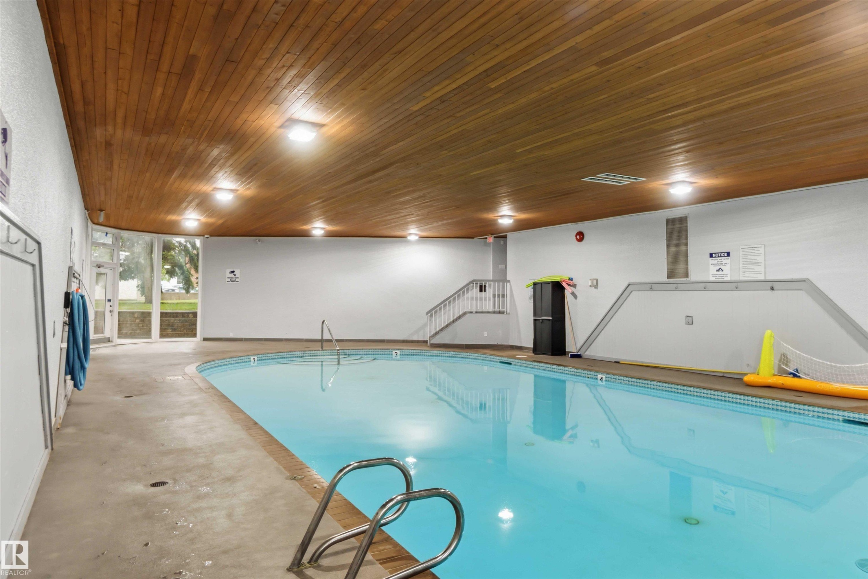 Indoor swimming pool featuring a wood-finish ceiling, perimeter lighting, and large windows - #121 5125 Riverbend Rd Nw Nw, Edmonton, AB - Indoor Photo Showing Other Room With In Ground Pool