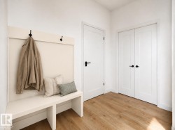 Built-in bench with integrated coat hooks, wood-finish flooring, and white paneled doors with matte black hardware - 